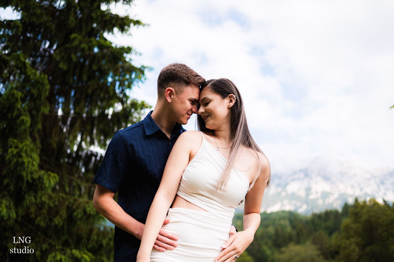 A couple in white and navy stands close together with mountains in the background.