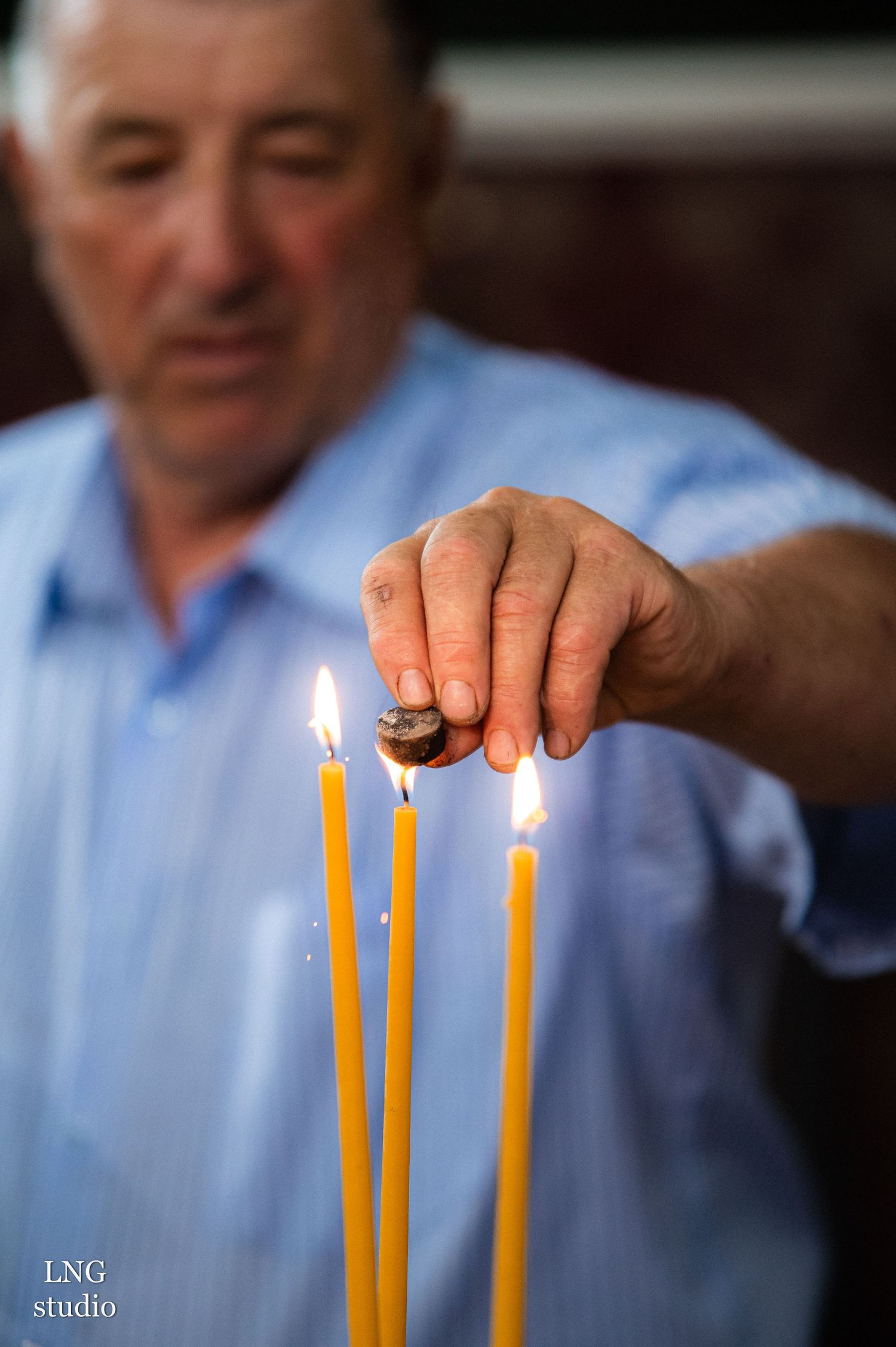 Hands holding lit yellow candles during a religious baptism ceremony.