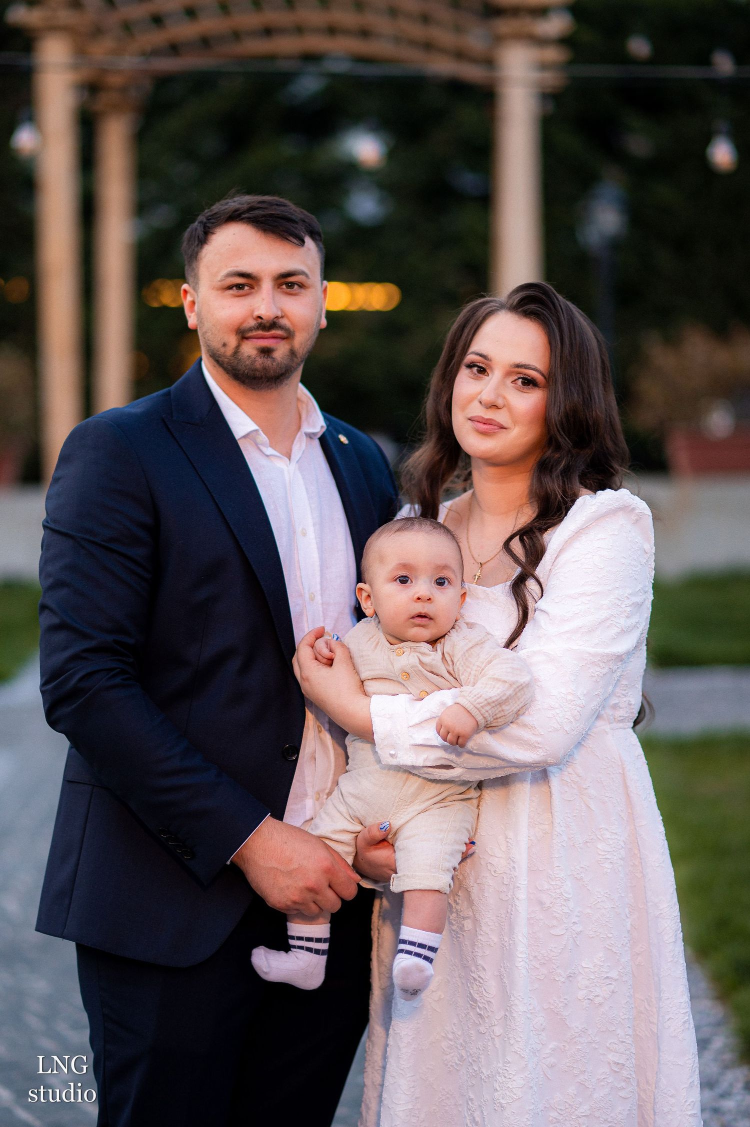 Elegant family portrait outdoors under a gazebo with decorative lighting.
