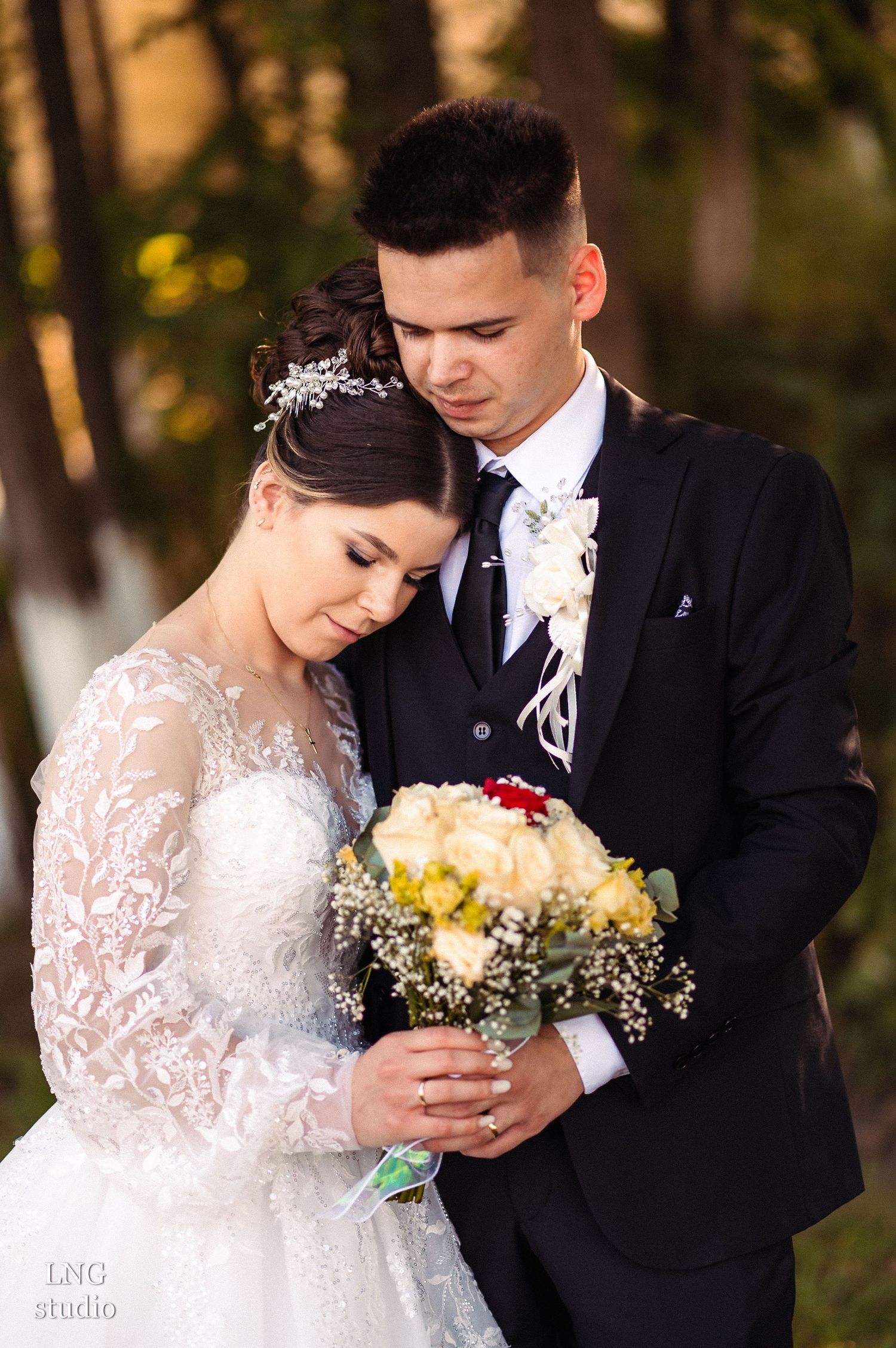 Romantic wedding portrait with couple admiring floral bouquet outdoors.