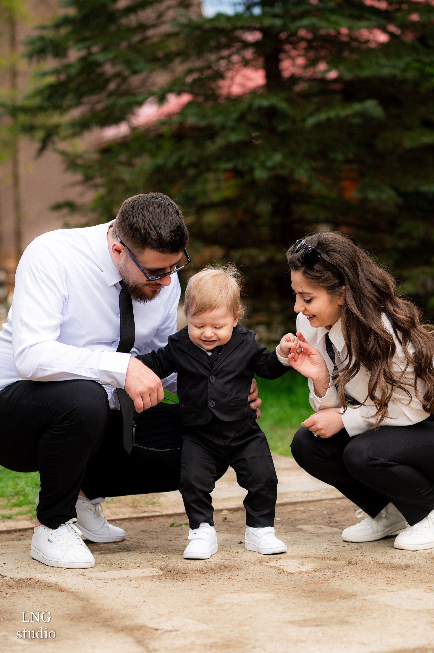 Family kneeling together on pathway sharing a playful moment in coordinated outfits.