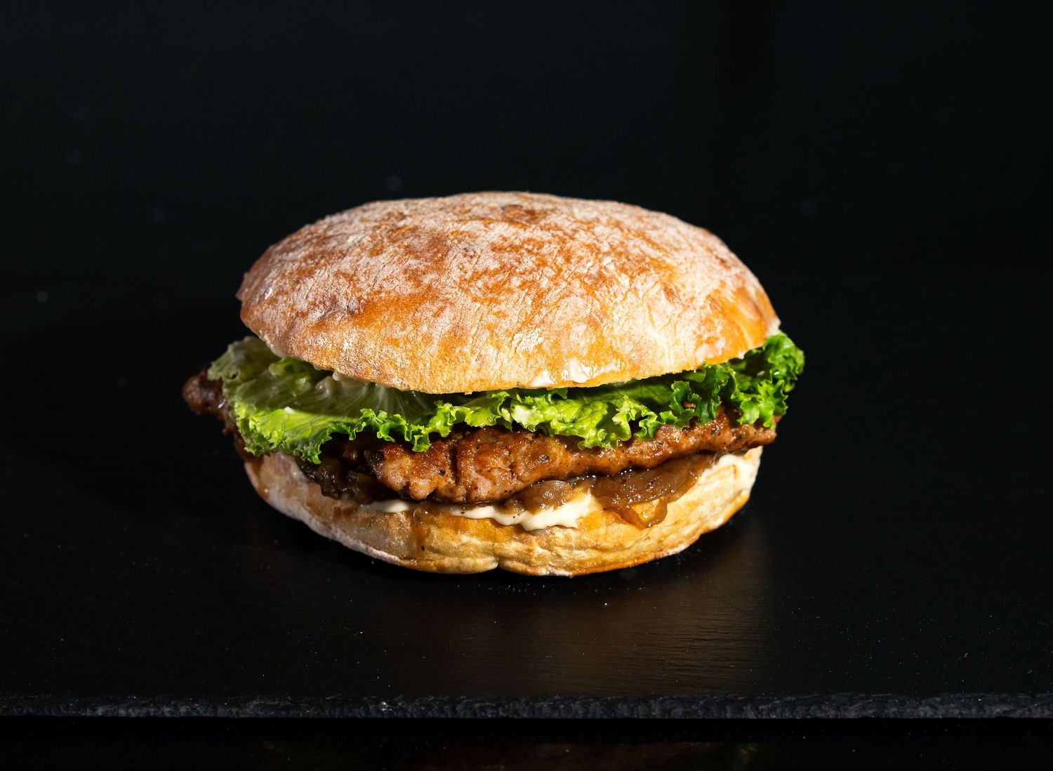 A classic hamburger with lettuce and sauce on a golden toasted bun against dark background.