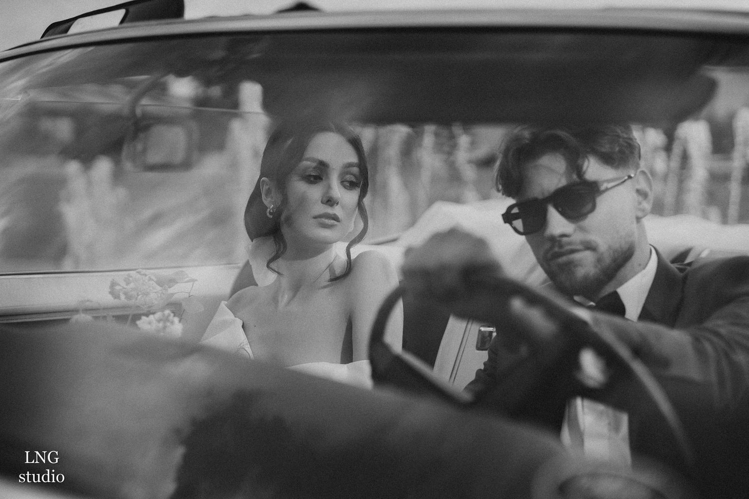 Vintage-style black and white photo showing a couple in a classic car with romantic film noir aesthetic.