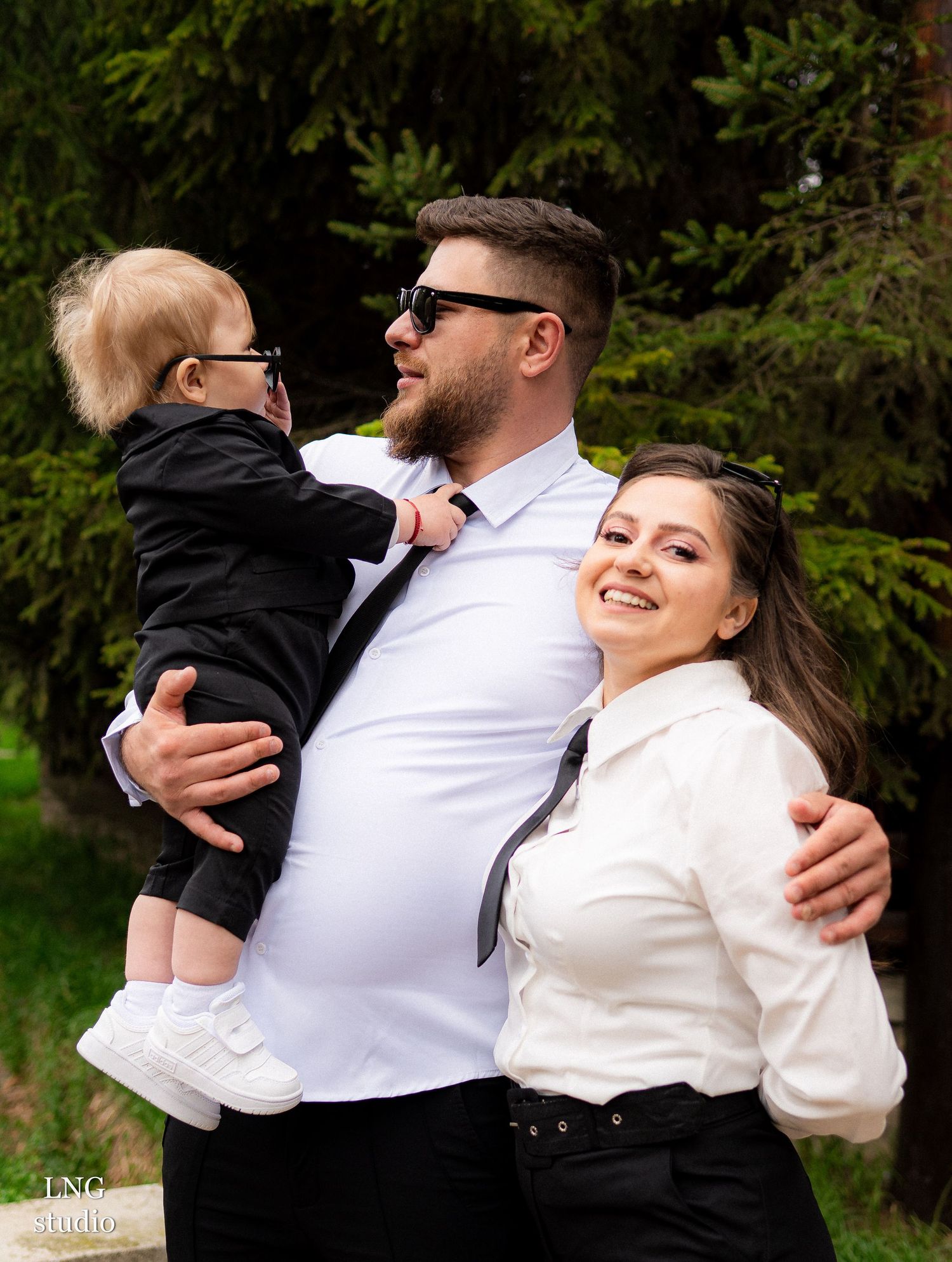 A stylish family portrait outdoors with coordinated black and white outfits against a natural green backdrop.