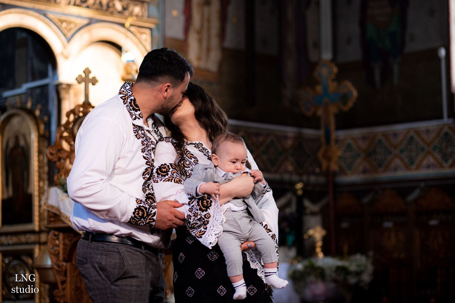Intimate family moment during a religious ceremony in a beautifully decorated Orthodox church.