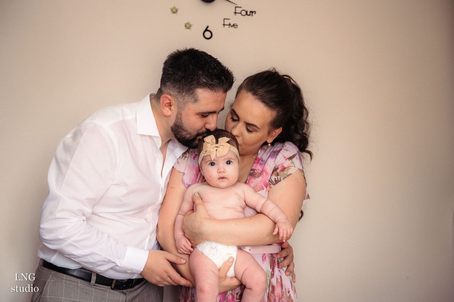 A family shares an intimate moment together against a beige wall with decorative clocks.