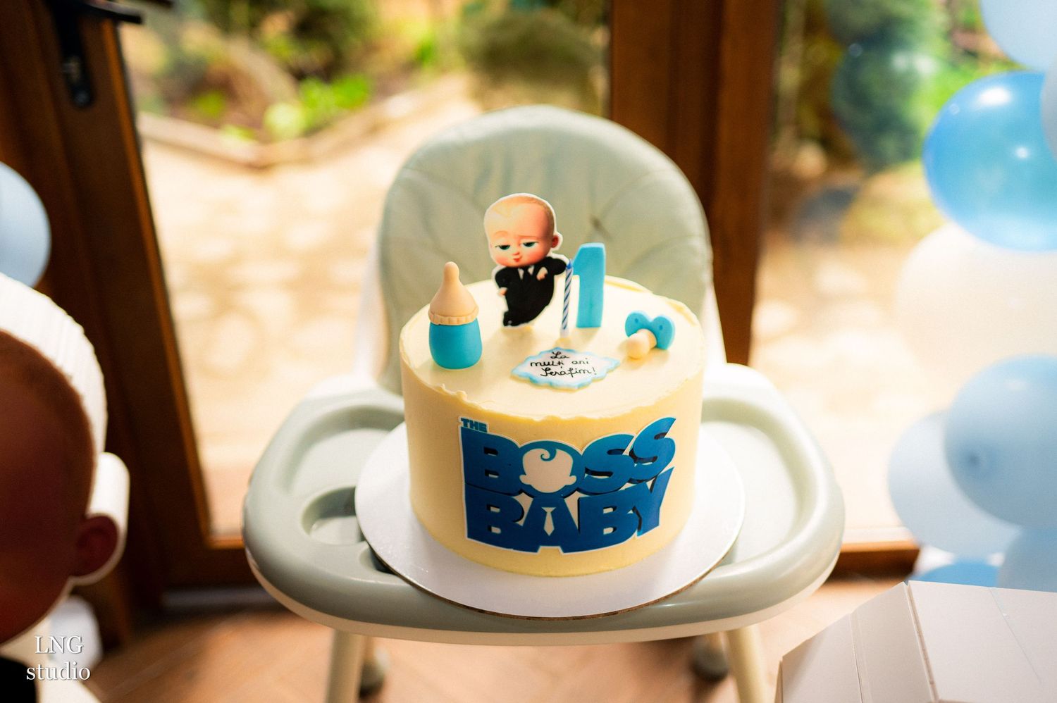 Blue and white birthday cake with Boss Baby themed topper on a high chair.