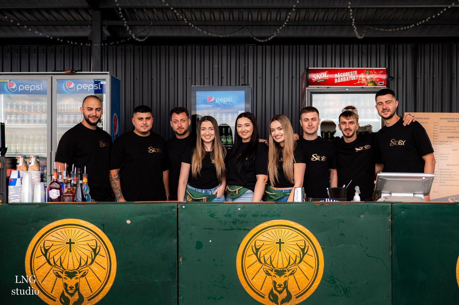 Staff members in black uniforms stand behind a bar counter with deer logo emblems.