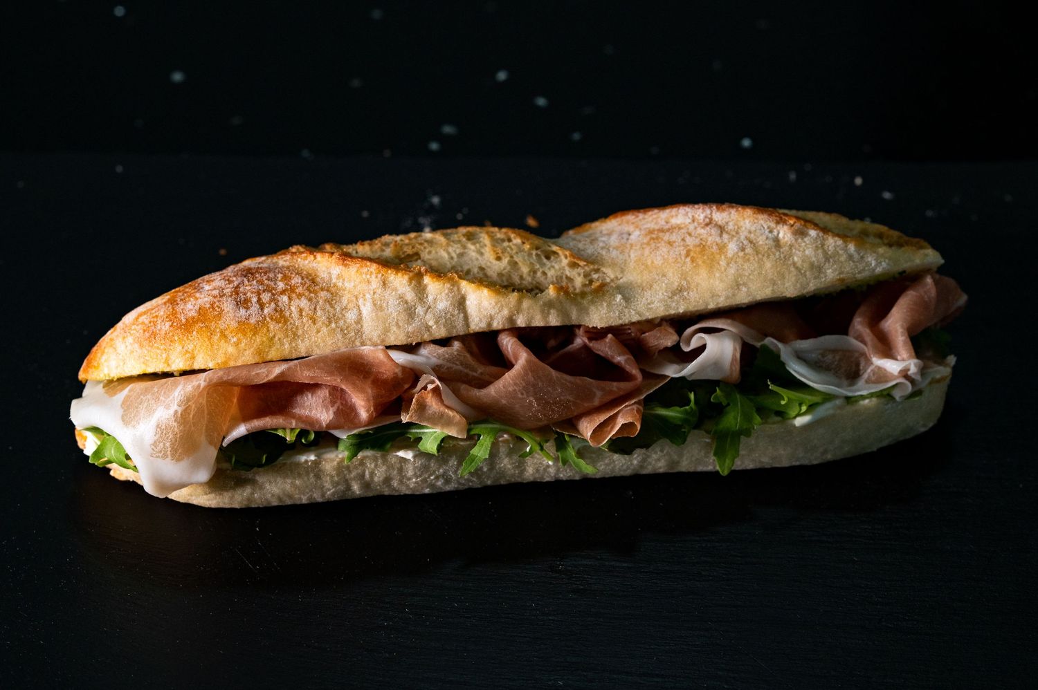 Submarine sandwich with meat, lettuce and tomatoes on crusty bread shot against dark background.