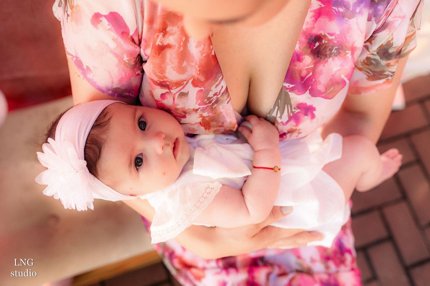 A baby wearing white clothing and a headband is held in floral patterned arms.