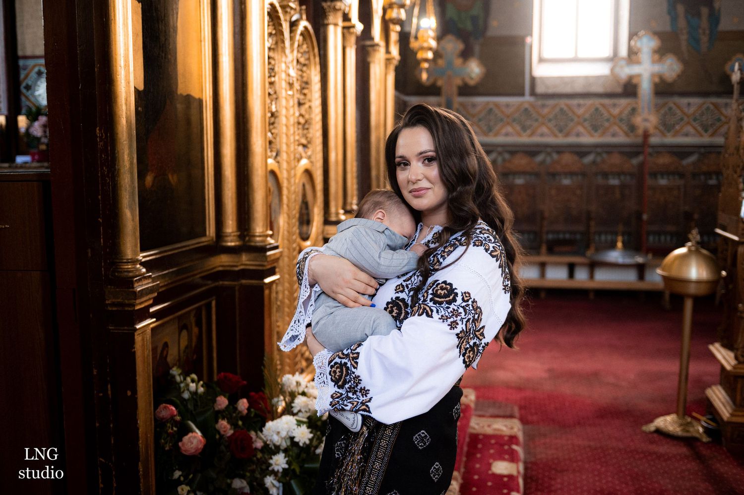 A christening ceremony in an ornate Orthodox church interior with traditional embroidered clothing.