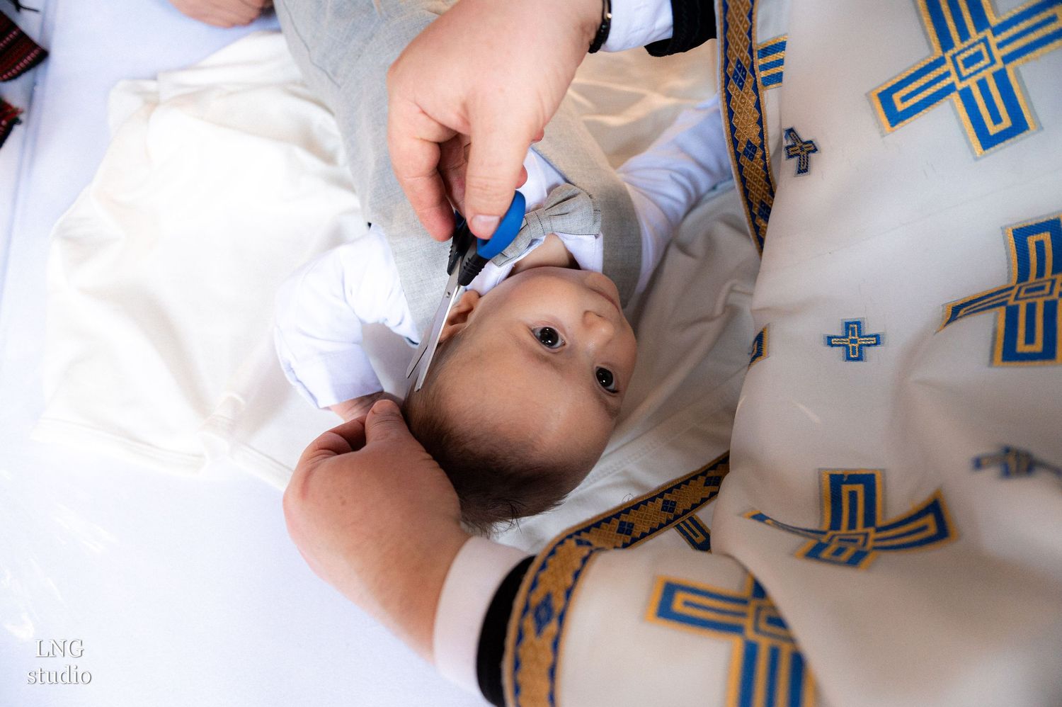 Baby in white clothing during Orthodox baptism ceremony with decorative crosses visible.