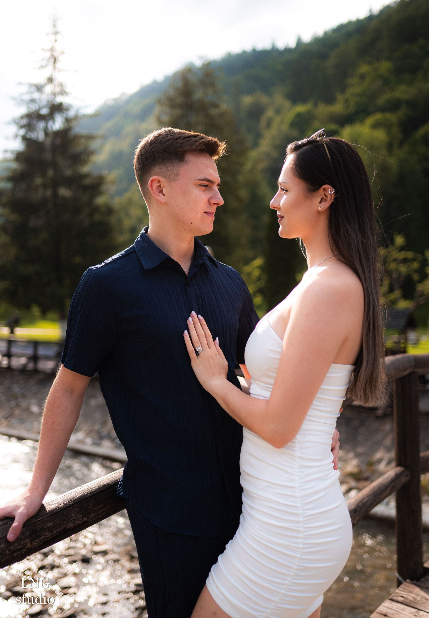 Couple shares affectionate moment by wooden railing in mountain setting.