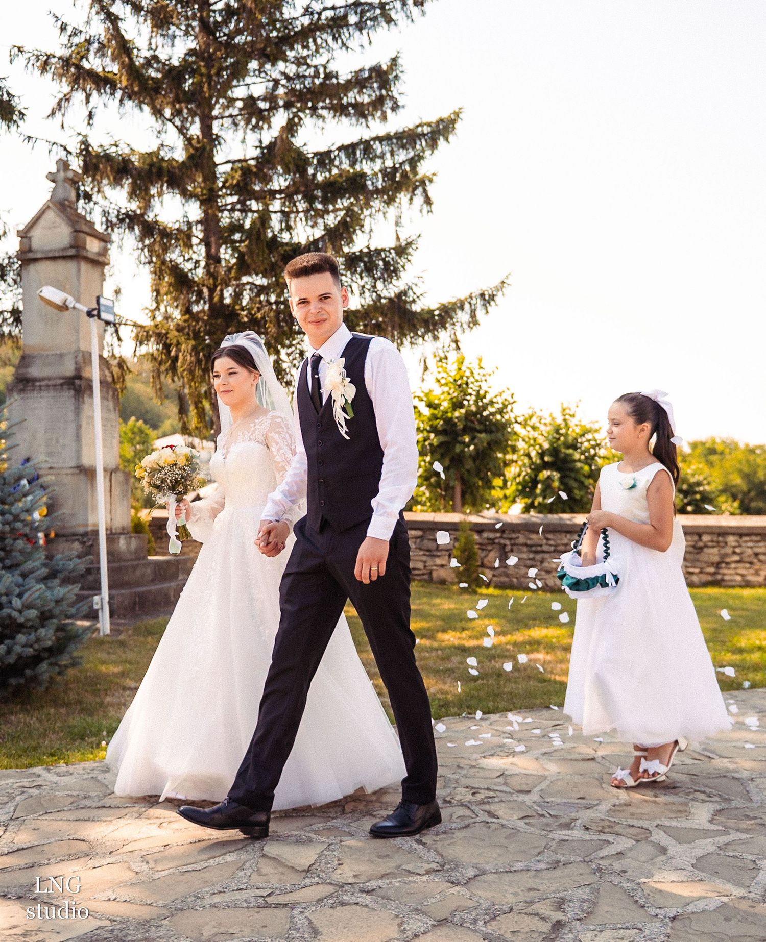 Wedding party walking on stone path with flower girl in white dress following behind.