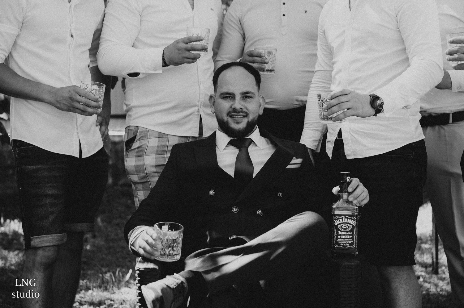 Black and white portrait of groomsmen sharing drinks during wedding celebration.