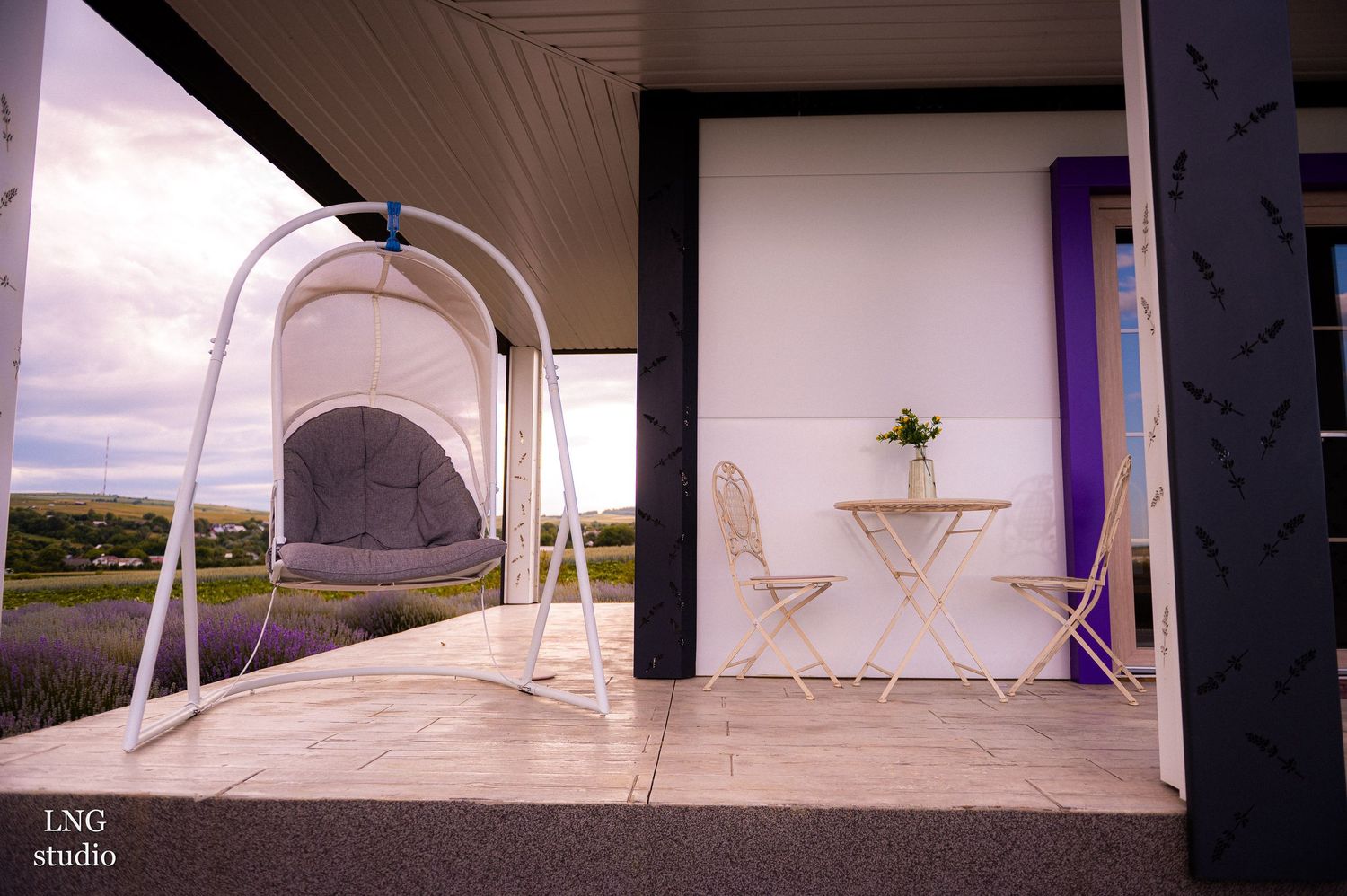 Hanging swing chair on a porch with white bistro set in background.