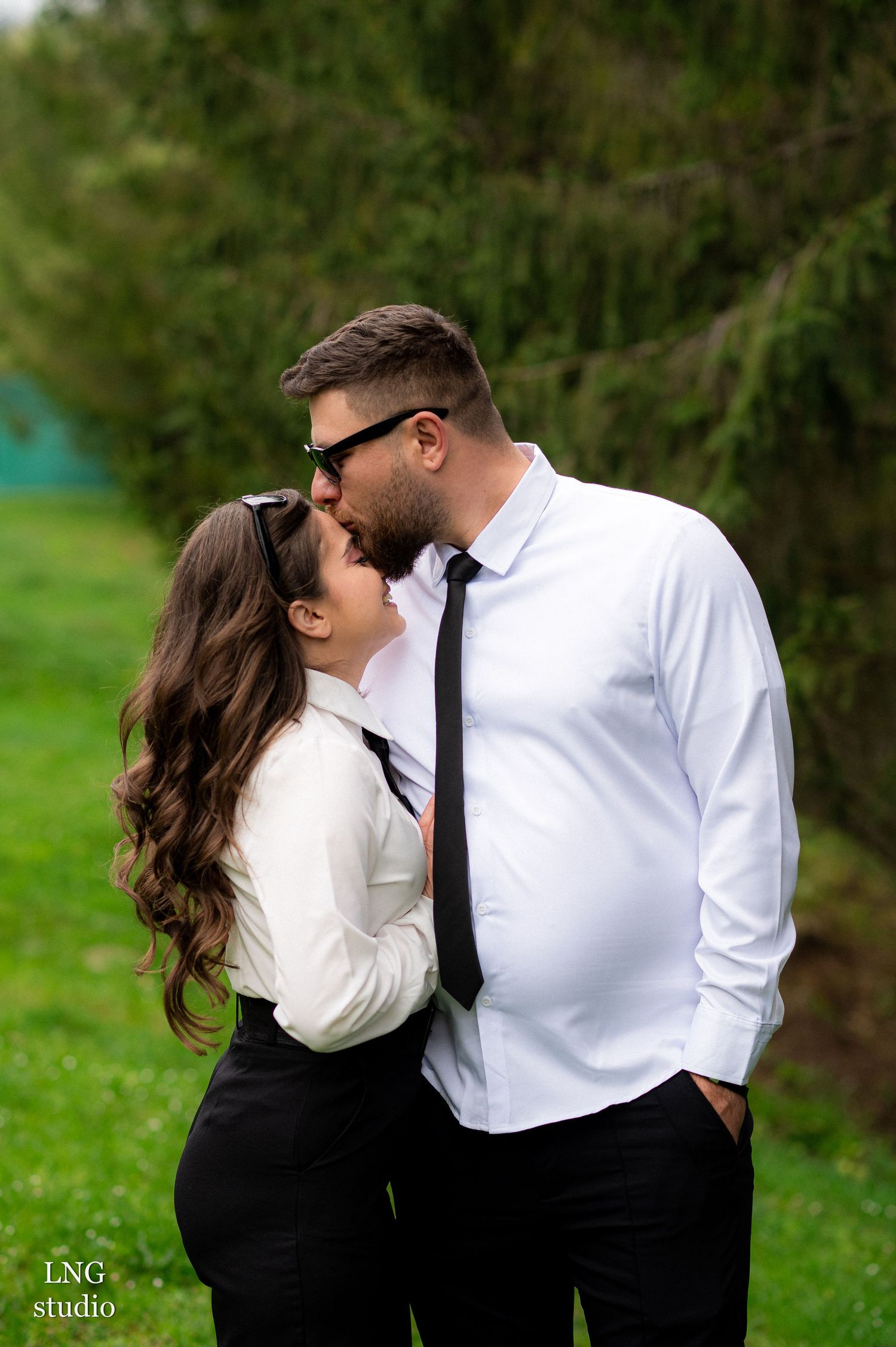 Romantic couple photoshoot in formal attire against natural green background.
