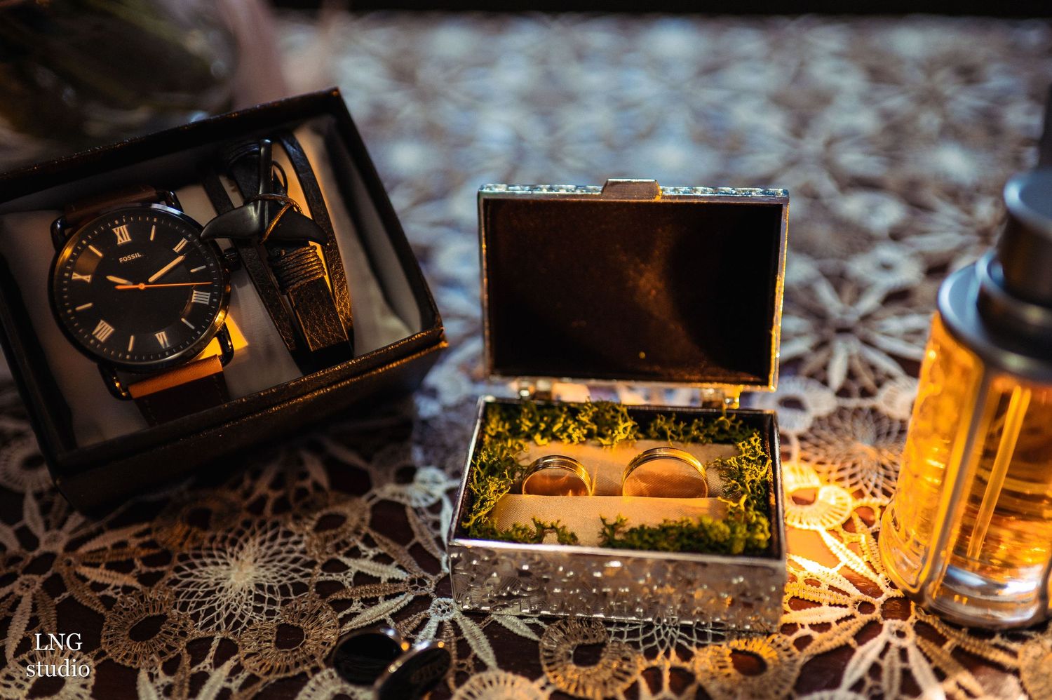 Wedding detail shot of watch, wooden box and whiskey bottle on patterned surface.