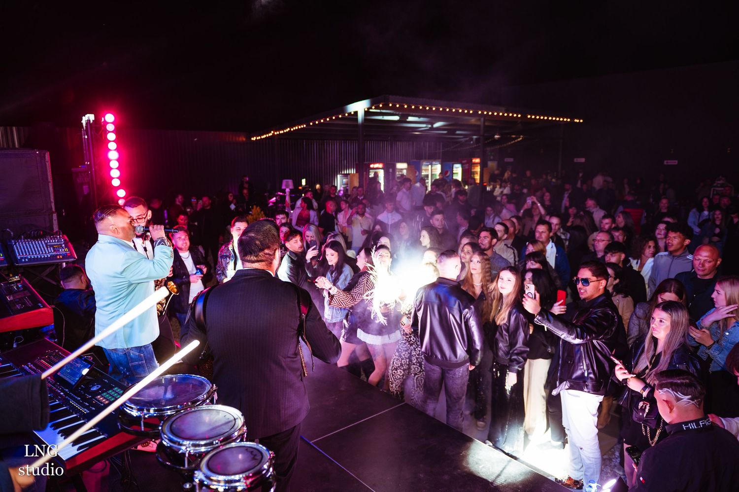 Panoramic view of a crowded nightclub event with colorful lighting and dancing silhouettes.
