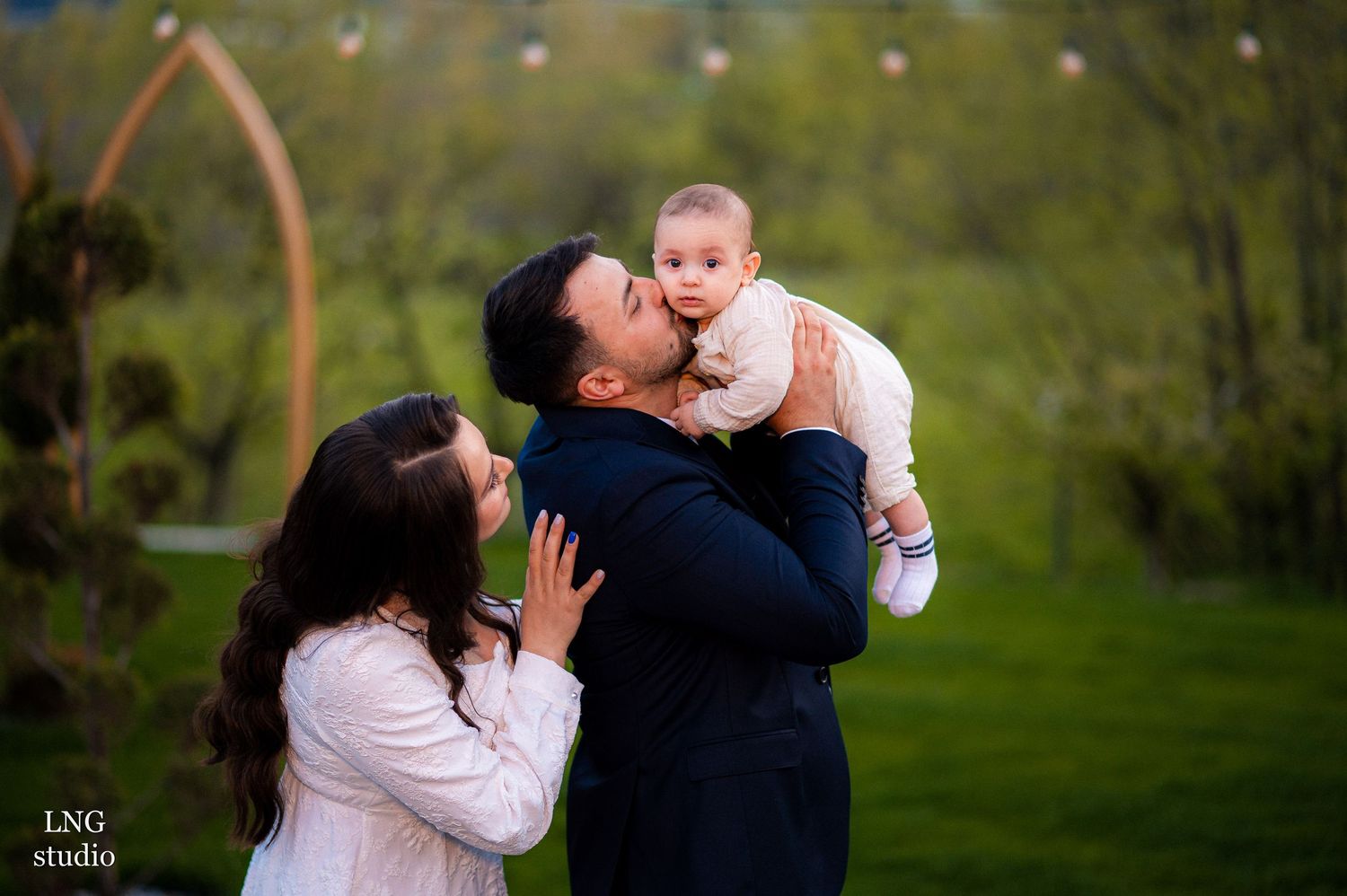 Joyful family moment captured outdoors with natural greenery and architectural elements.