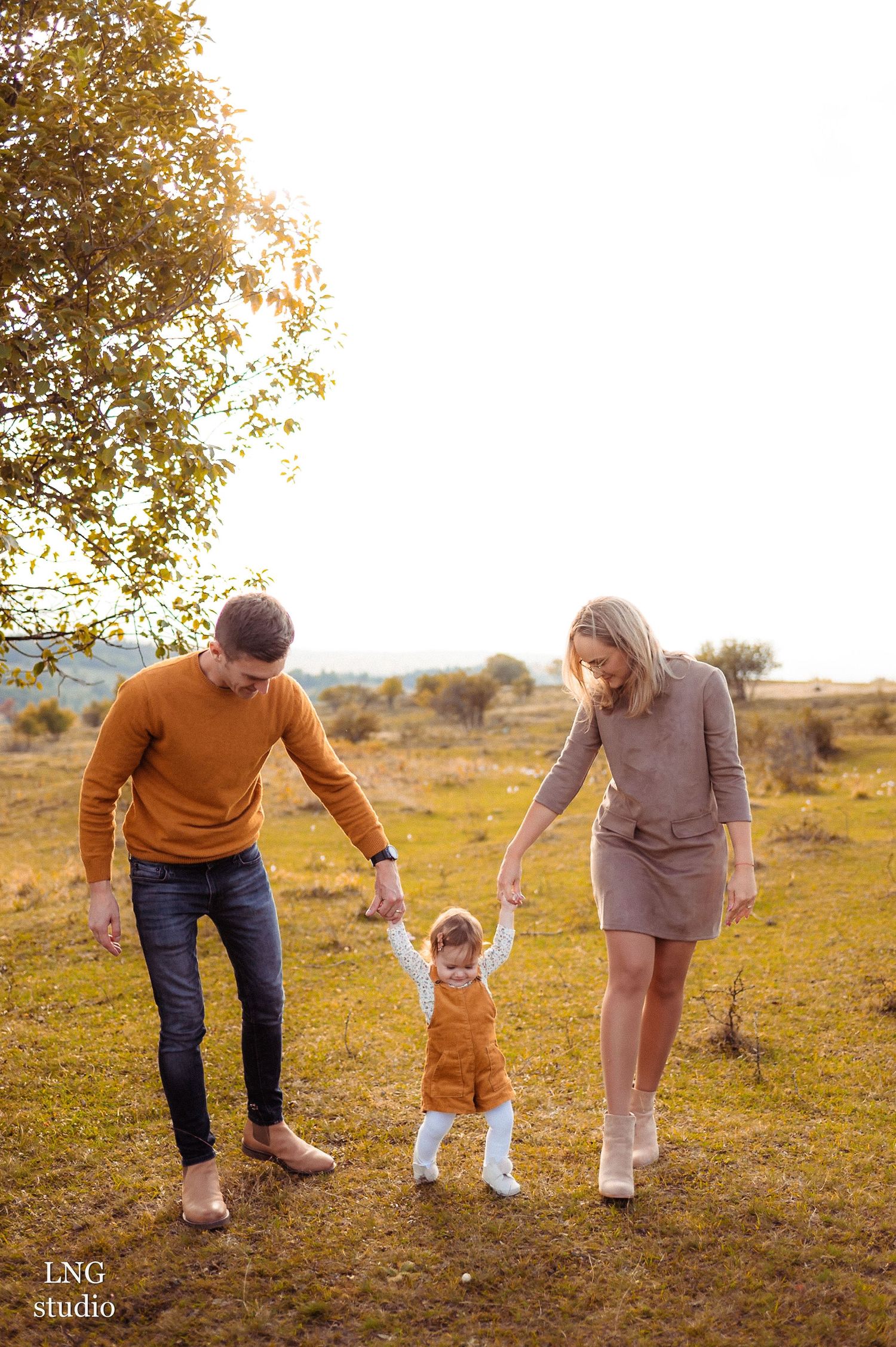 Family walks together holding hands in golden autumn field during sunset.