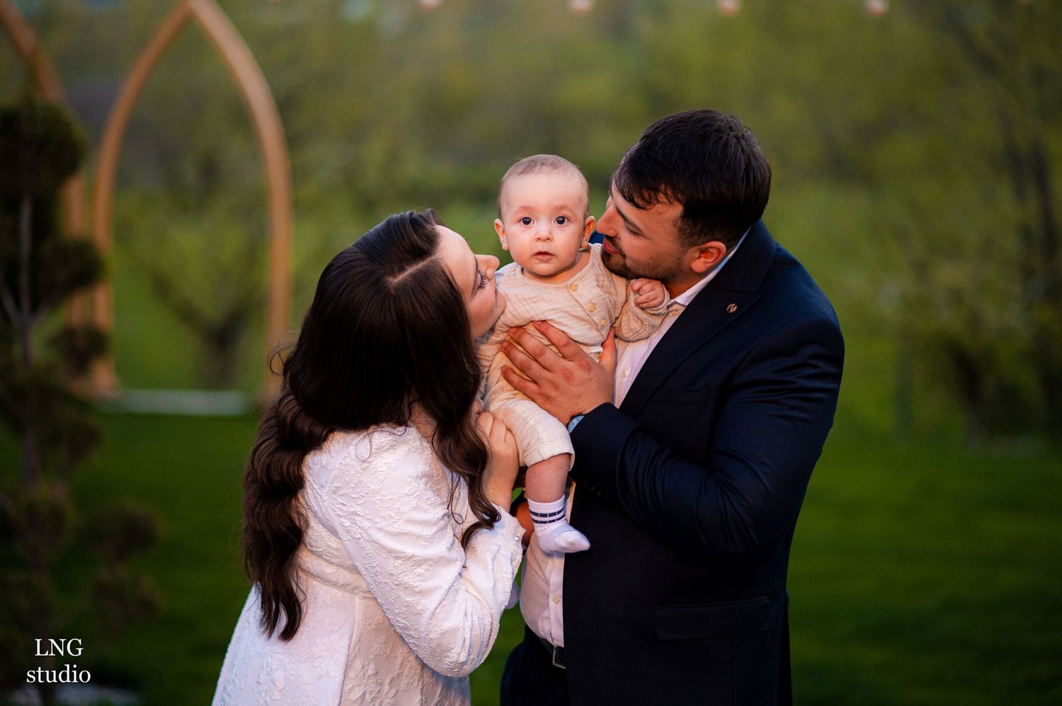 Intimate family portrait outdoors with garden arches and natural scenery in the background.