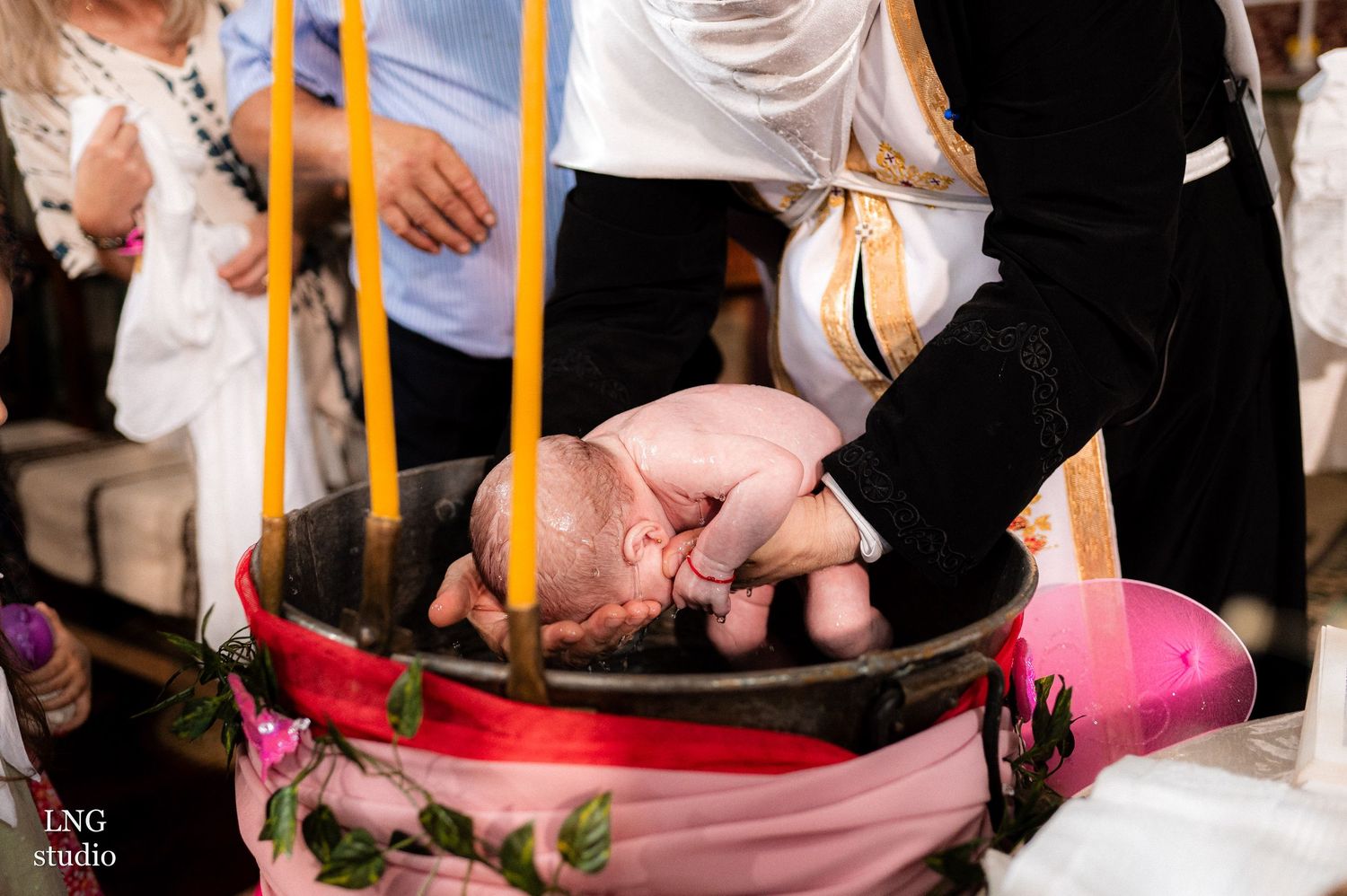 Clergy performing baptism ceremony with candles and traditional pink and white garments.