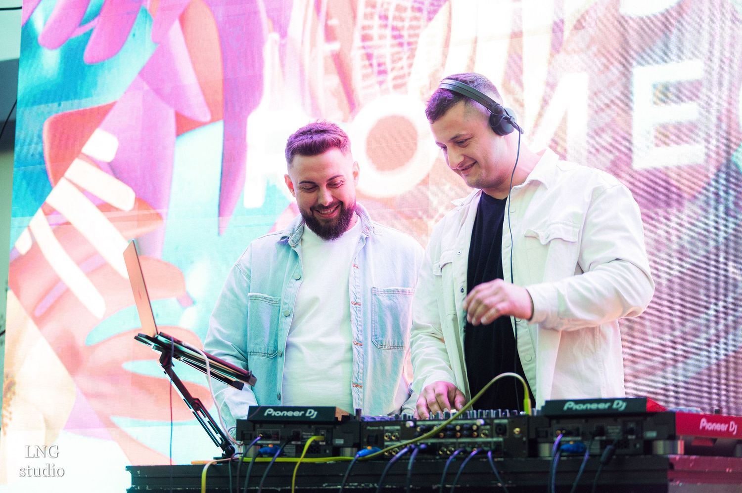 DJs perform at an electronic music event with vibrant pink lighting and professional equipment.