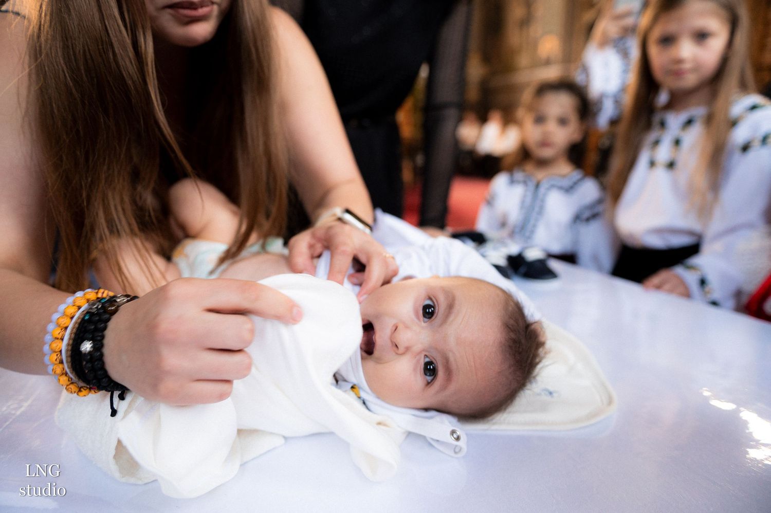 Baby in white baptismal gown lying on ceremonial table during Orthodox christening.