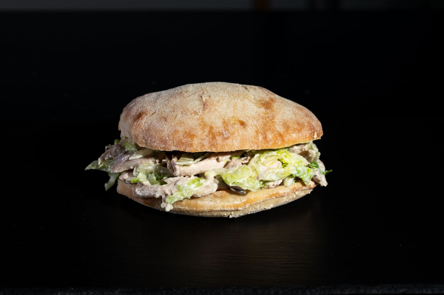 A classic chicken salad sandwich on rustic bread against a dark background.
