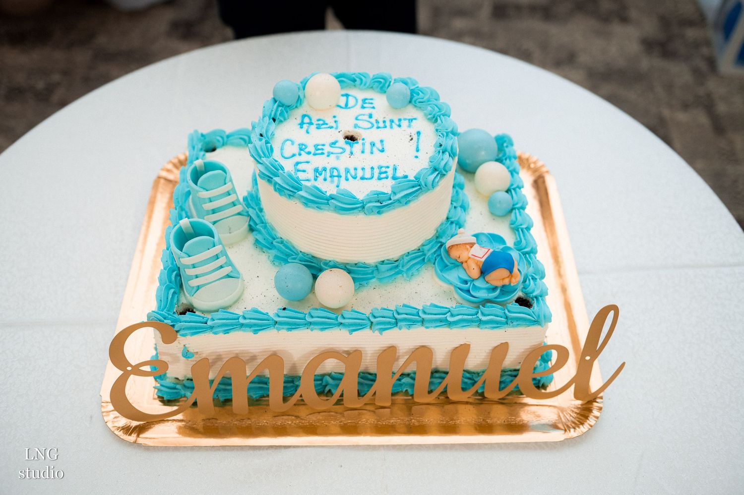 A blue and white tiered celebration cake with decorative elements on a gold cake board.