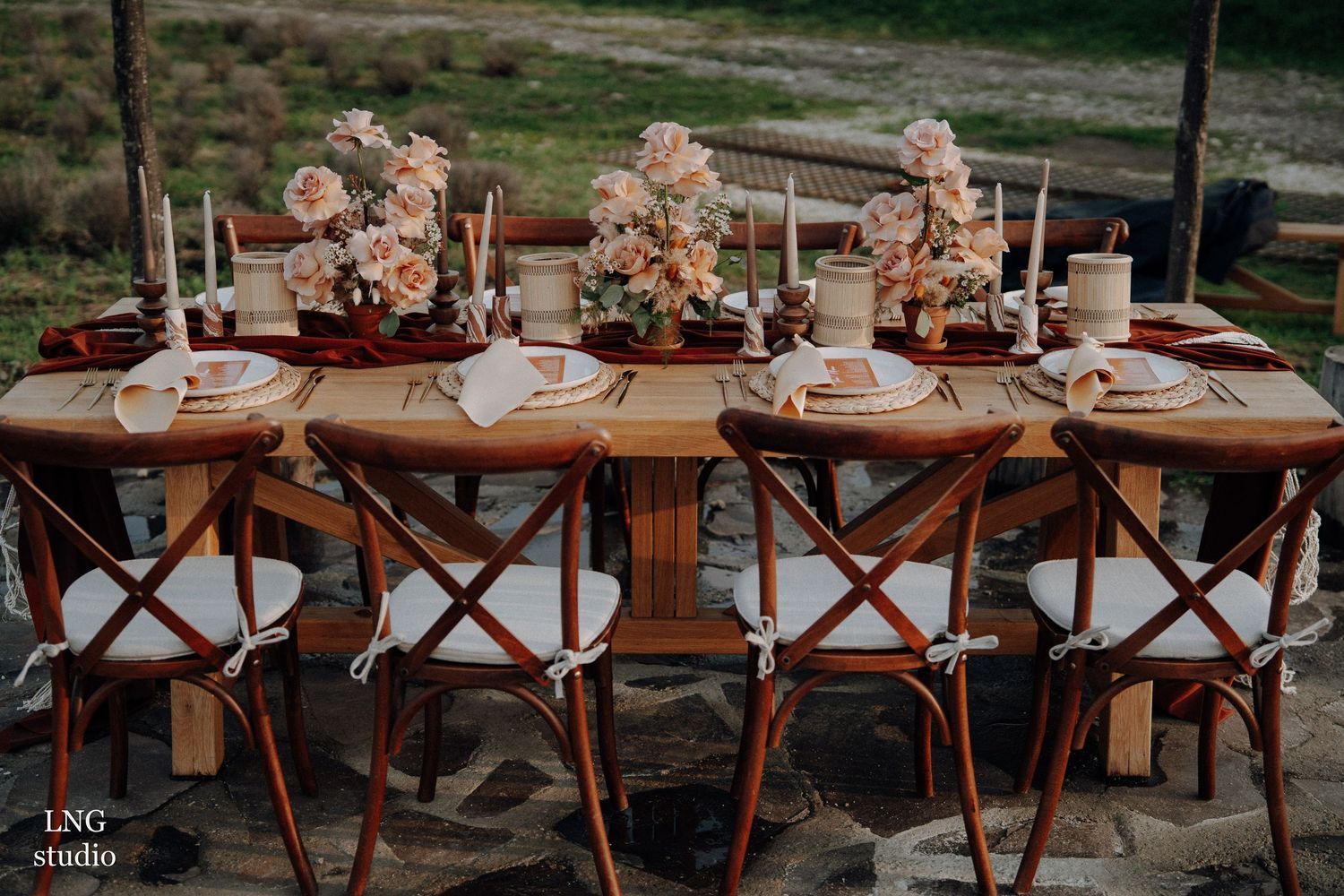 Rustic wooden dining tables with elegant place settings and floral centerpieces for an outdoor wedding reception.