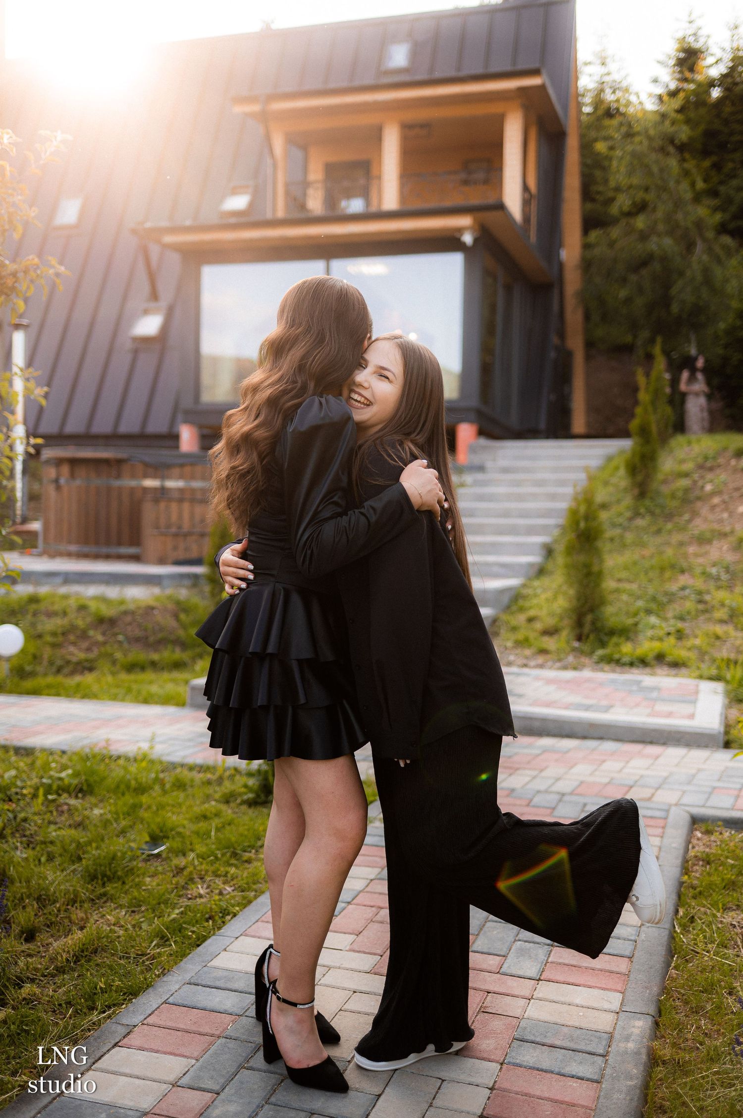 Two people share a tender embrace during an outdoor photoshoot on a brick walkway in front of a modern building.