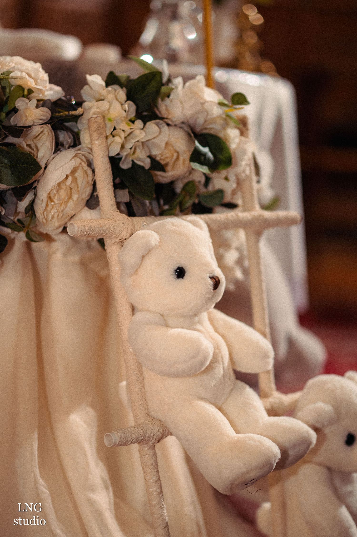 White plush teddy bear decoration with floral arrangements on a table.