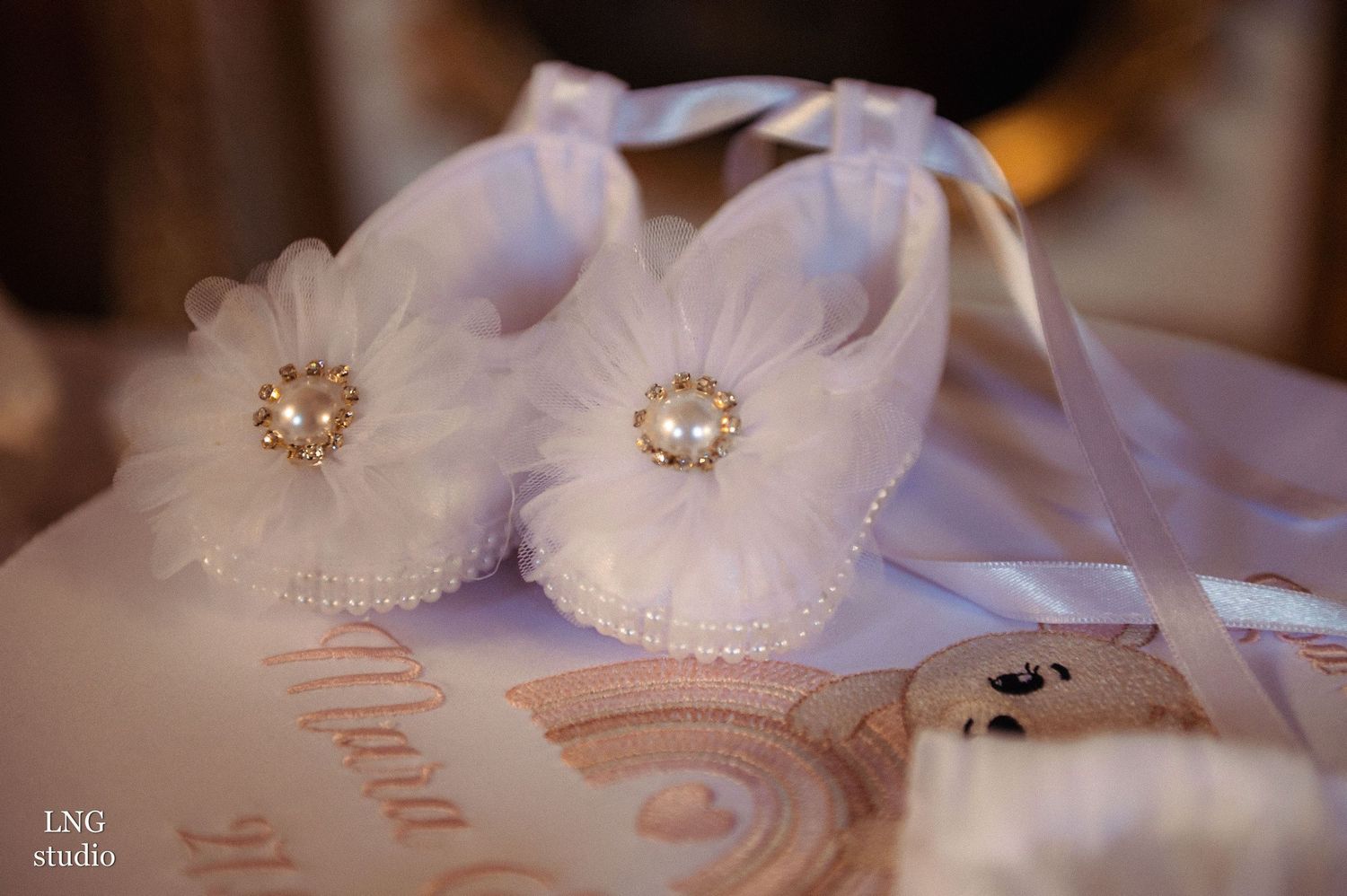 Delicate white baby shoes with pearl embellishments displayed on decorative paper.