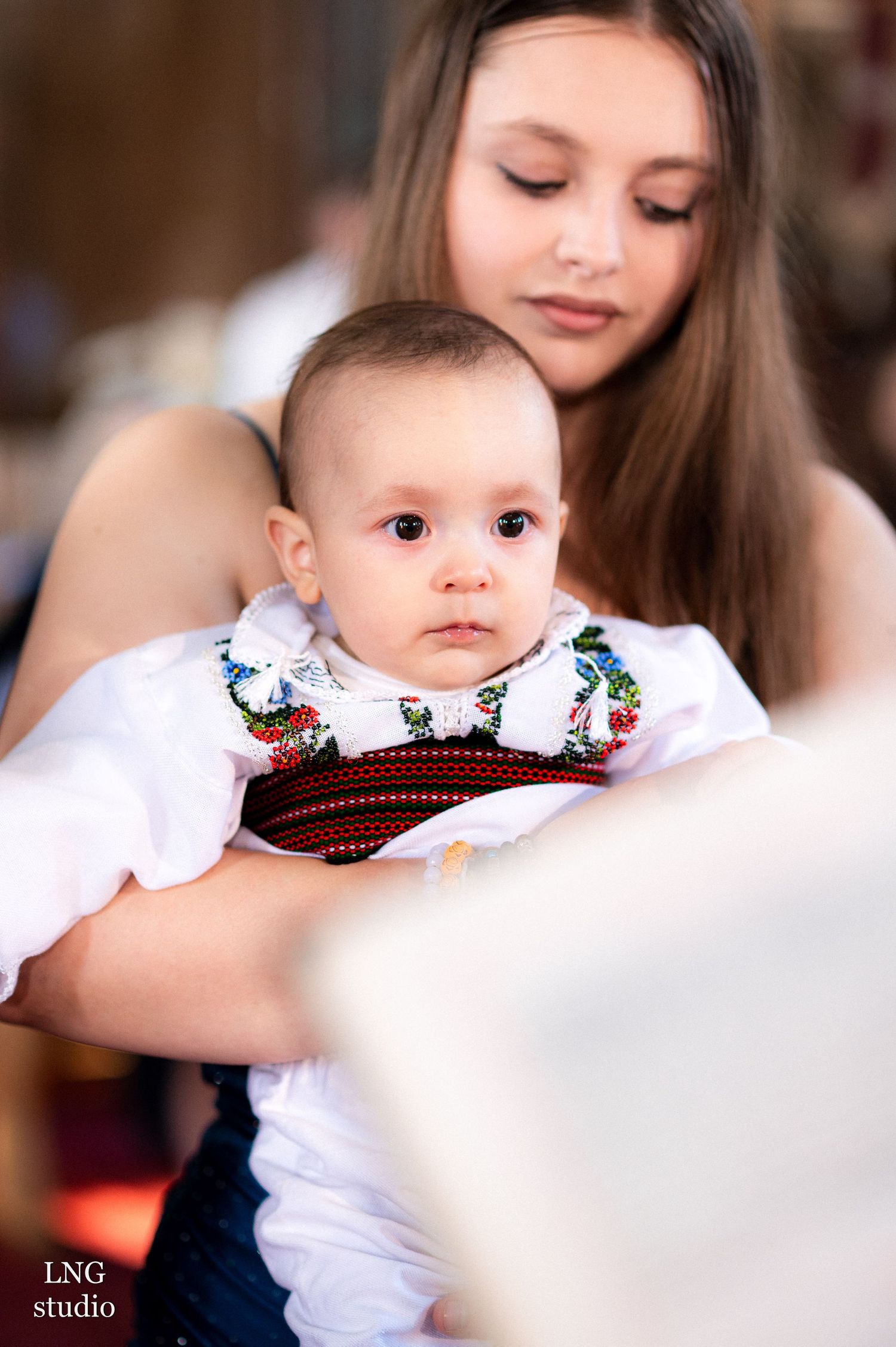 A young child in traditional white clothing with embroidered details at a cultural event.