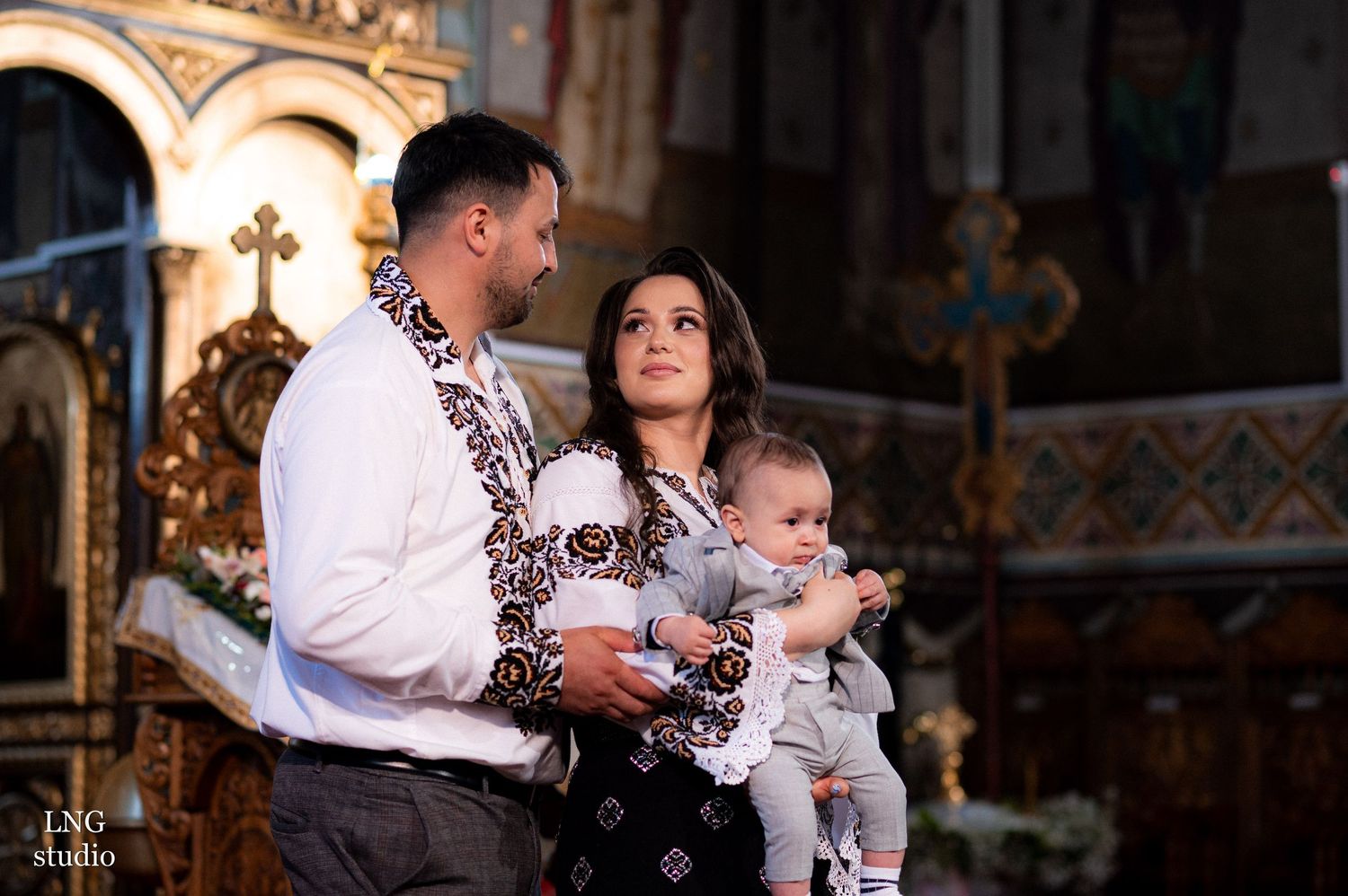 Family in matching embroidered attire celebrates a religious ceremony in an ornate church interior.