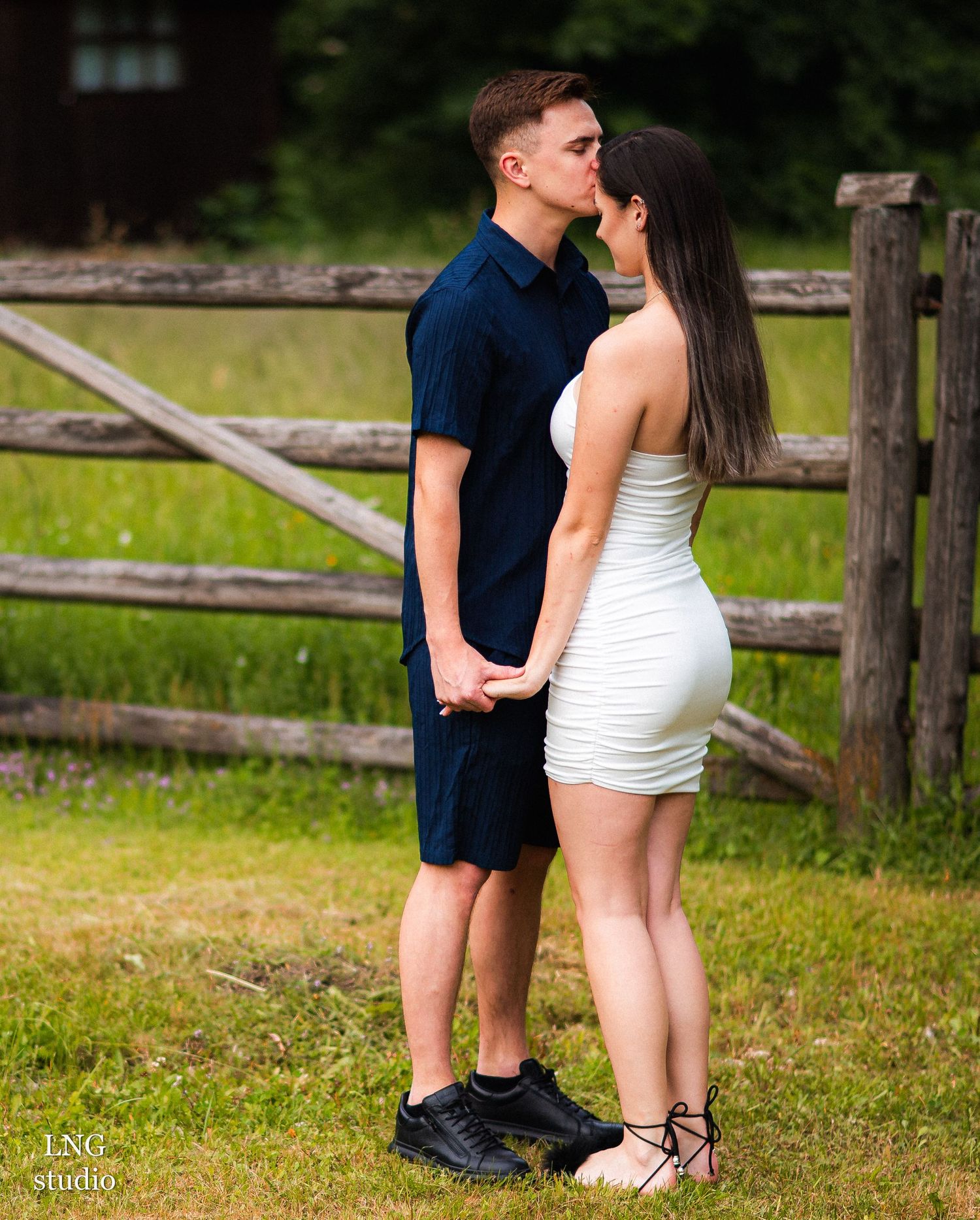 Couple in coordinated outfits poses playfully by wooden fence.