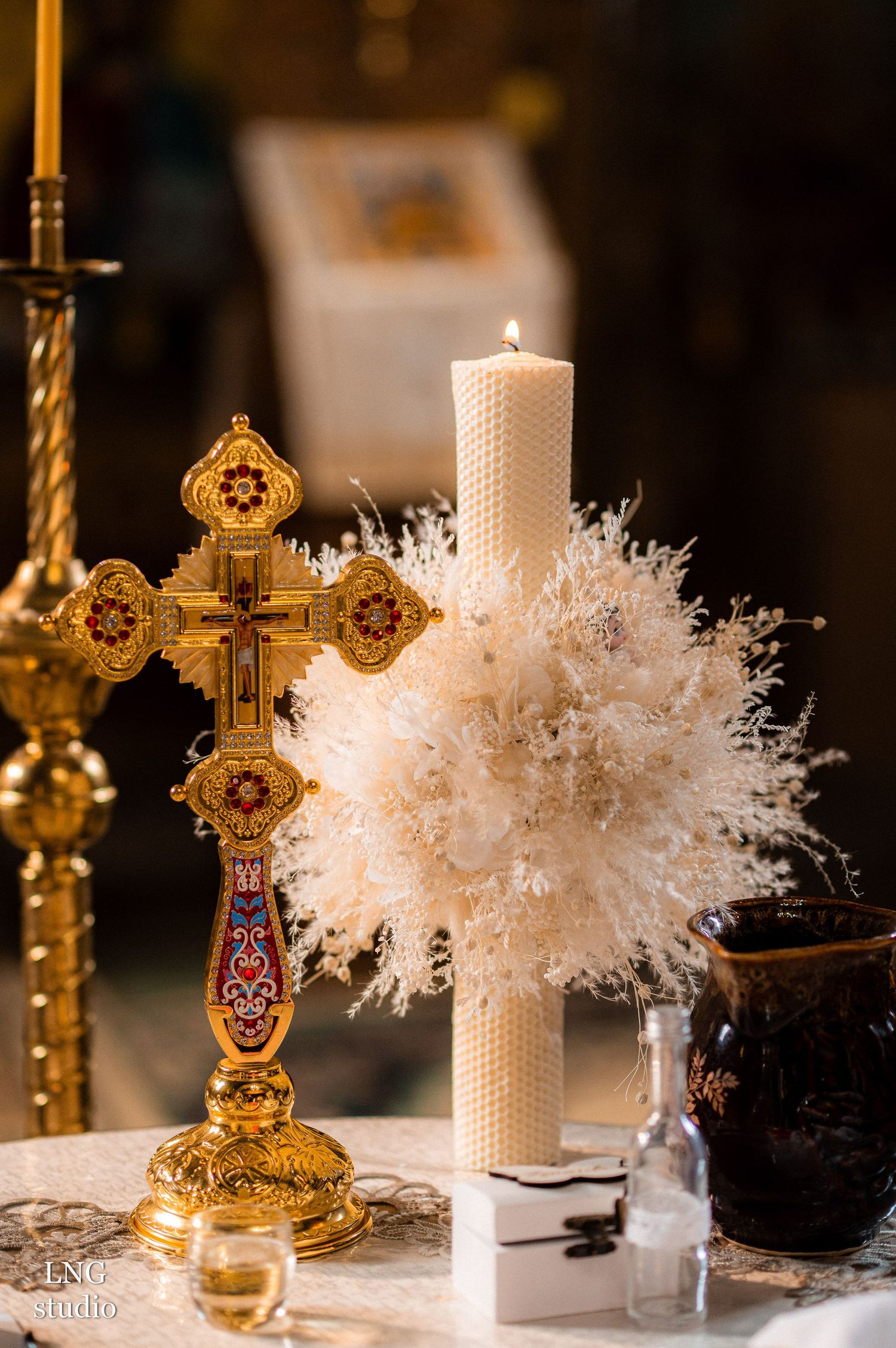 Ornate golden cross and white candle with decorative elements on ceremonial table.