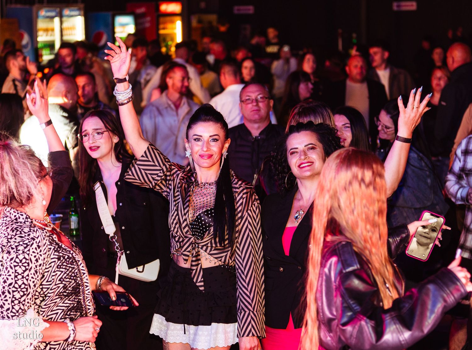 Enthusiastic crowd at nightclub with red lighting and leopard print outfits.