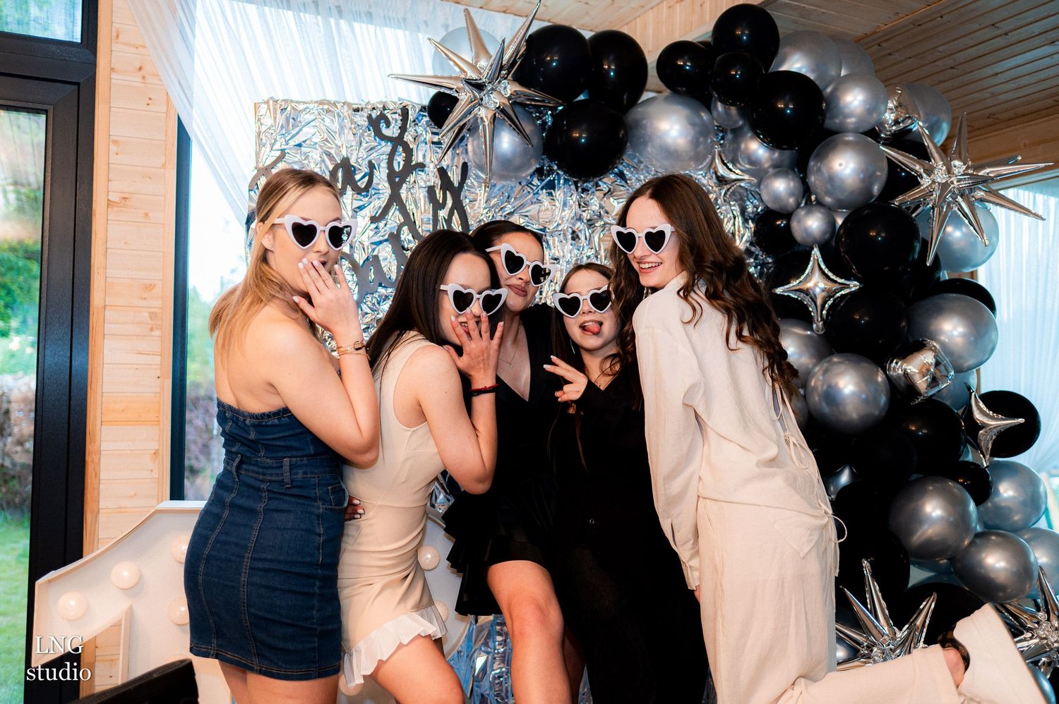 Group celebrates at a party with black and silver balloon arch decorations in background.