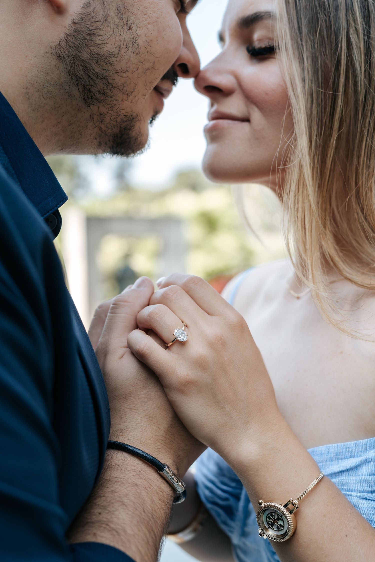 Couple holding hands closely, woman wearing diamond engagement ring and gold watch, sharing a romantic moment.