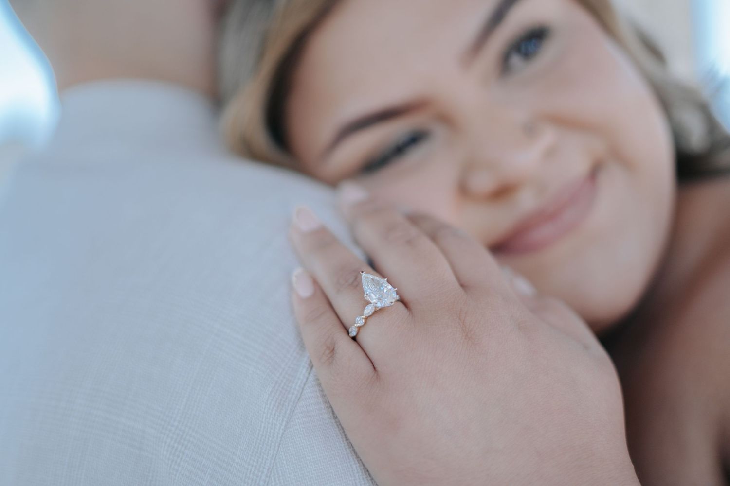 Smiling bride showing off pear-shaped diamond engagement ring with halo setting while embracing her partner.