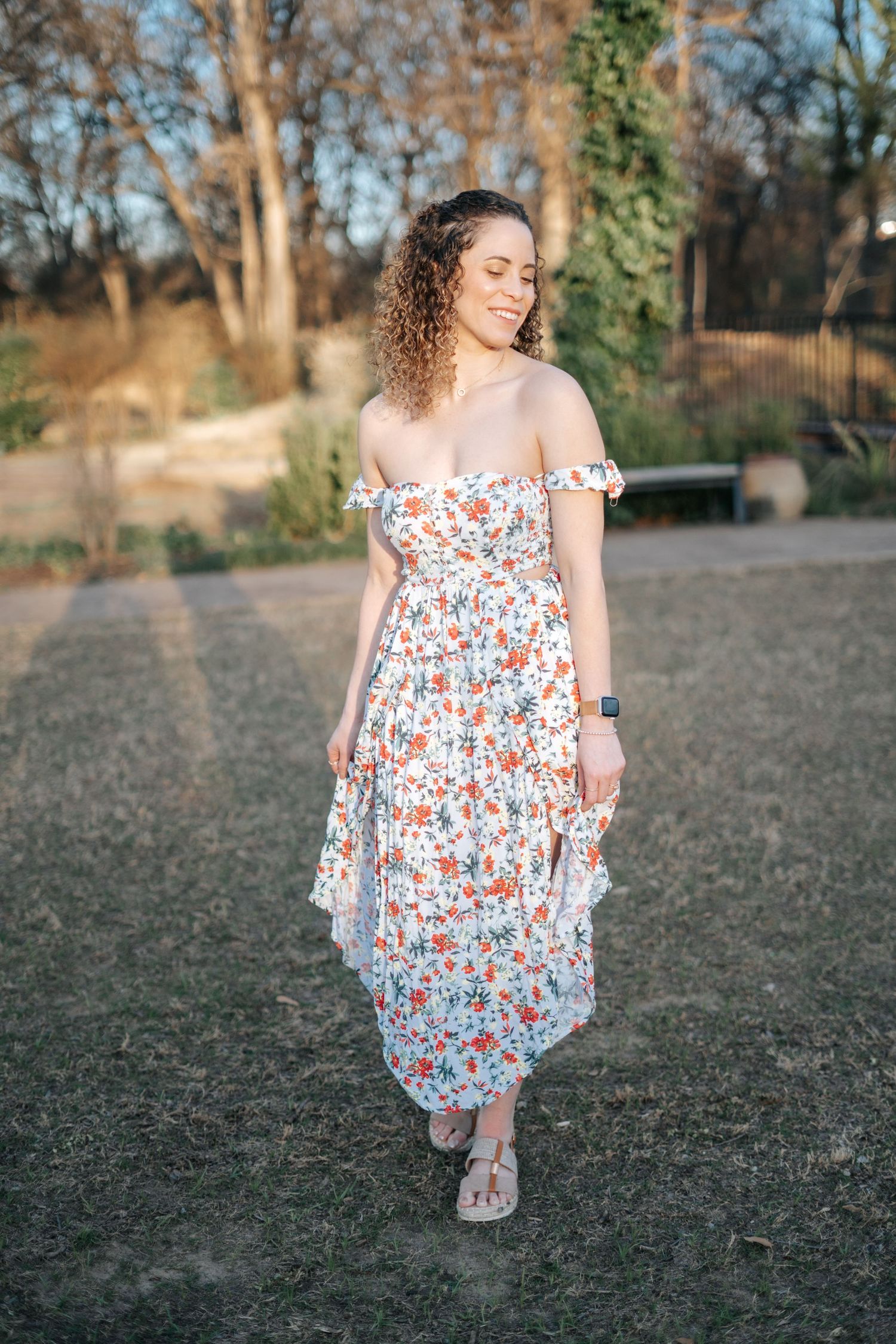 Woman in floral off-shoulder maxi dress walking outdoors in golden hour sunlight.