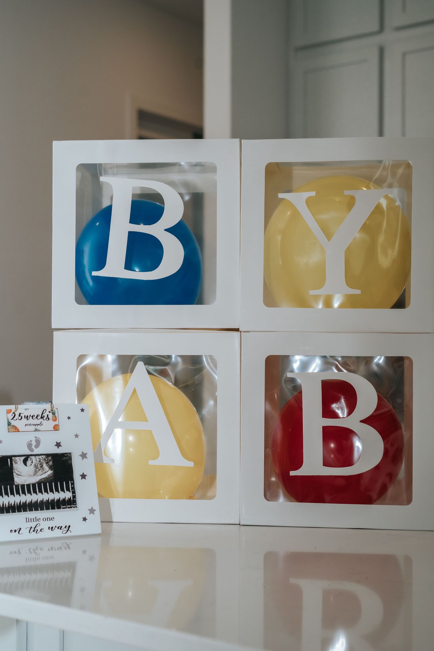 Baby shower balloon boxes spelling baby in blue, yellow, and red with ultrasound photo nearby.