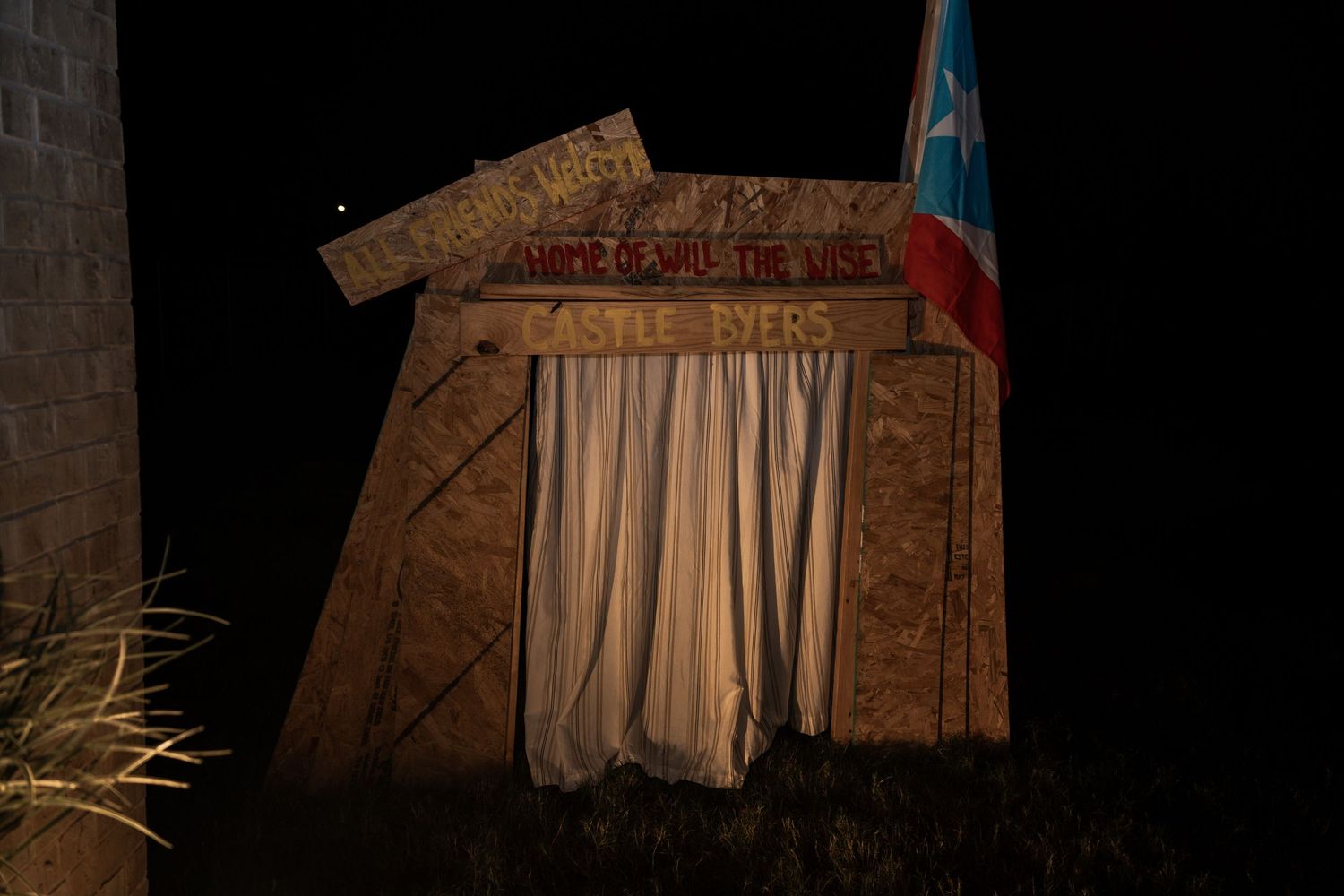 Nighttime view of Castle Ivers wooden structure with Puerto Rico flag and white curtains illuminated in darkness.
