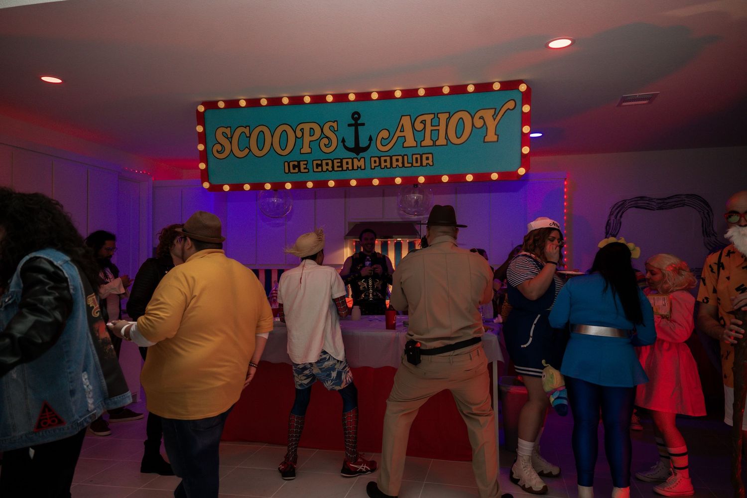 Guests in costumes gather at Scoops Ahoy ice cream parlor replica from Stranger Things at a themed event.