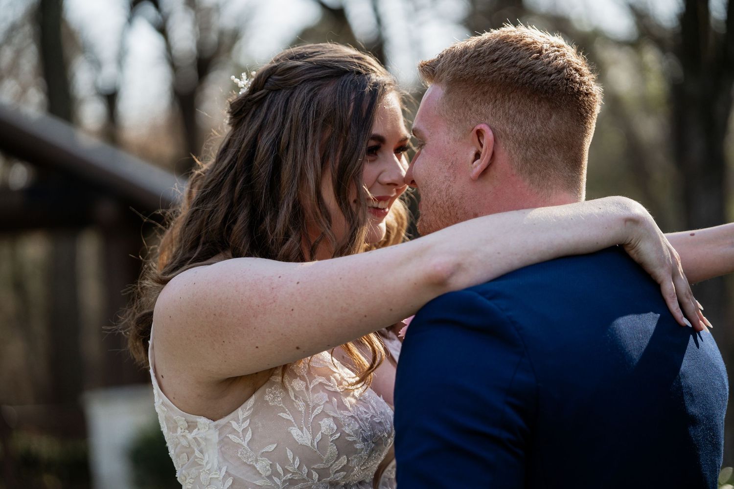 A bride and groom share a romantic embrace outdoors, smiling at each other during their wedding day.
