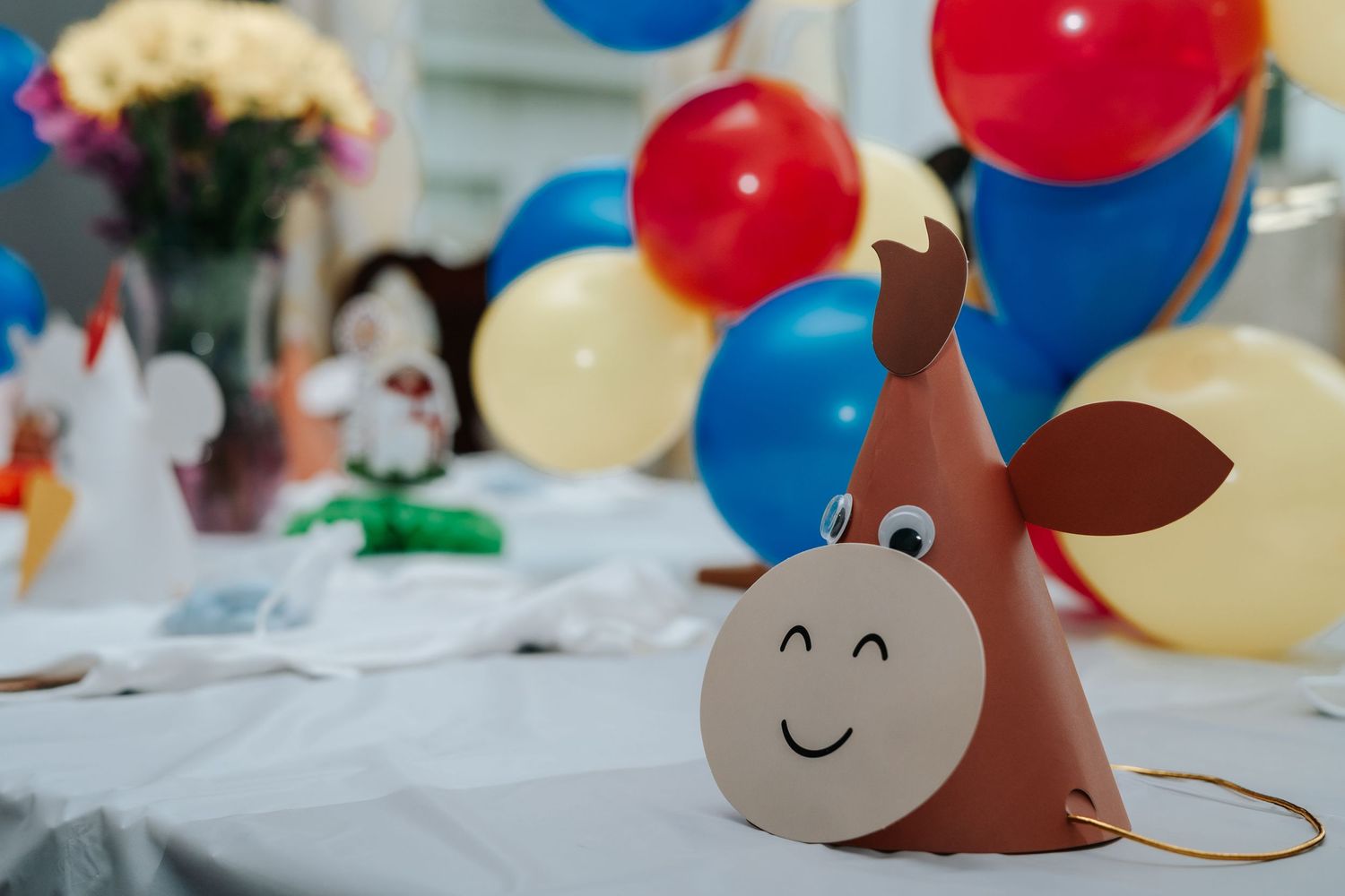 A cute horse-shaped birthday party hat on a table with colorful balloons in the background.