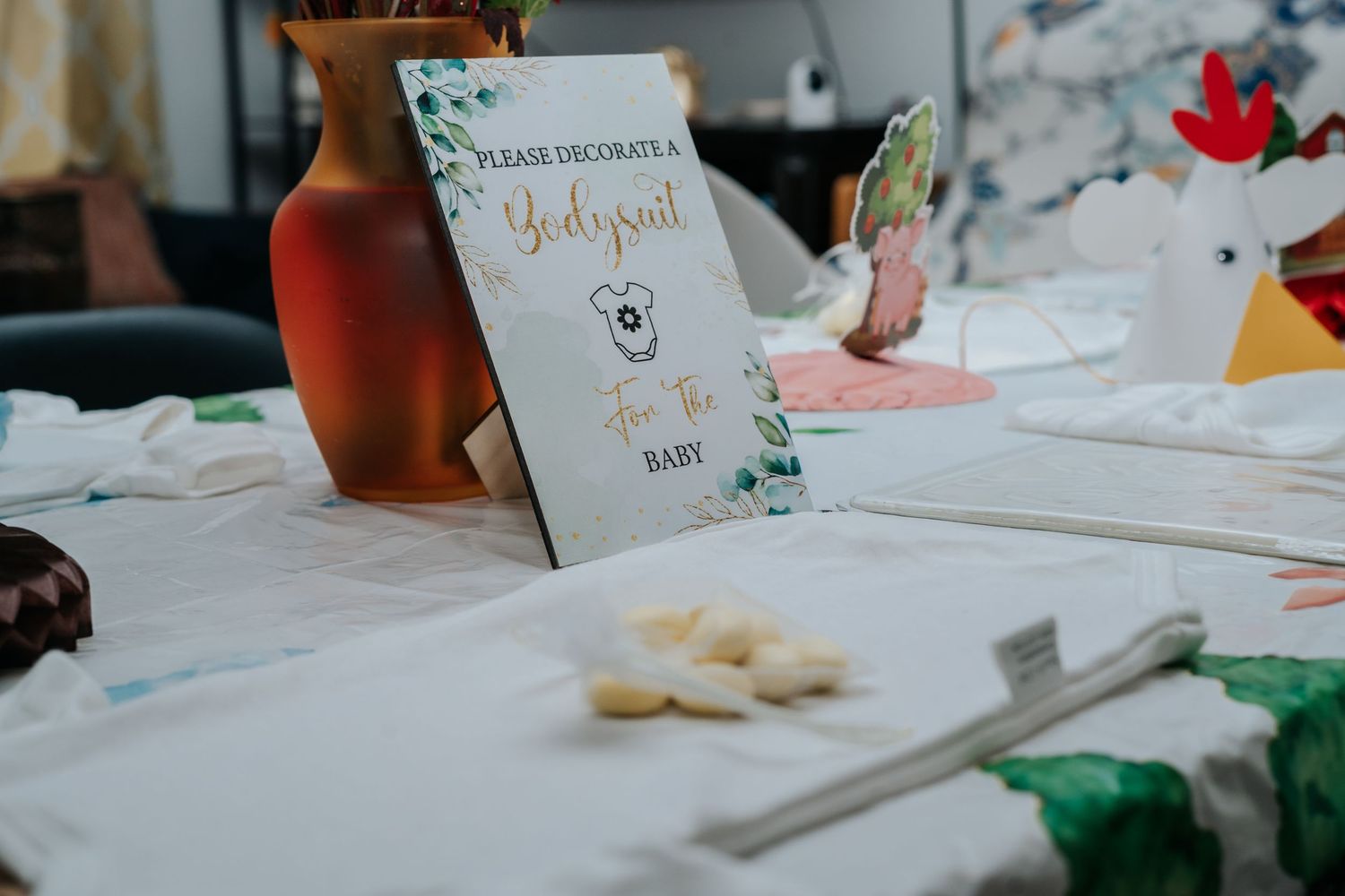 Baby shower table with a decorate a onesie sign, craft supplies, and festive decorations for a baby shower activity.